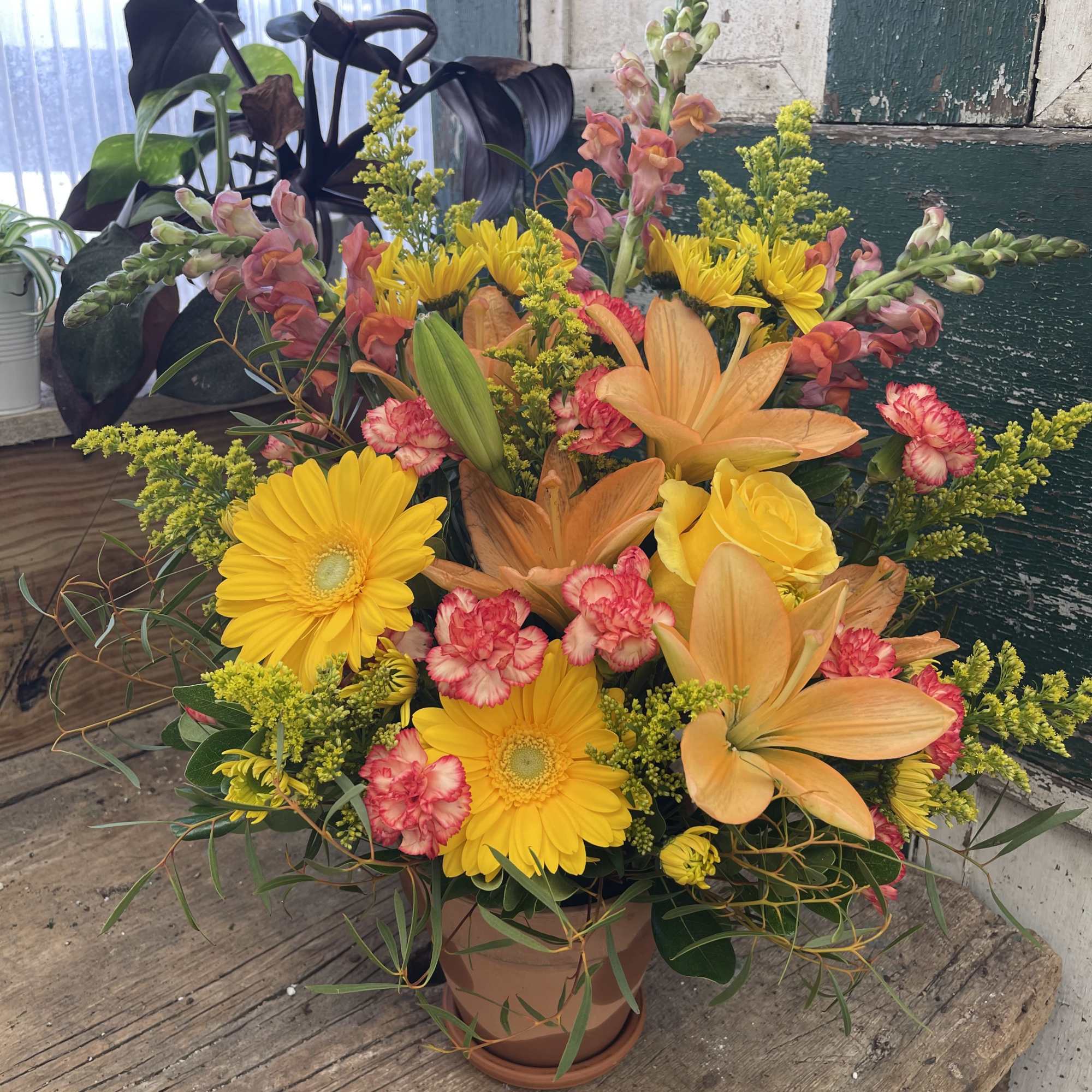Mixed bouquet with yellow daisies, orange lilies, pink carnations, and a yellow rose in a pot