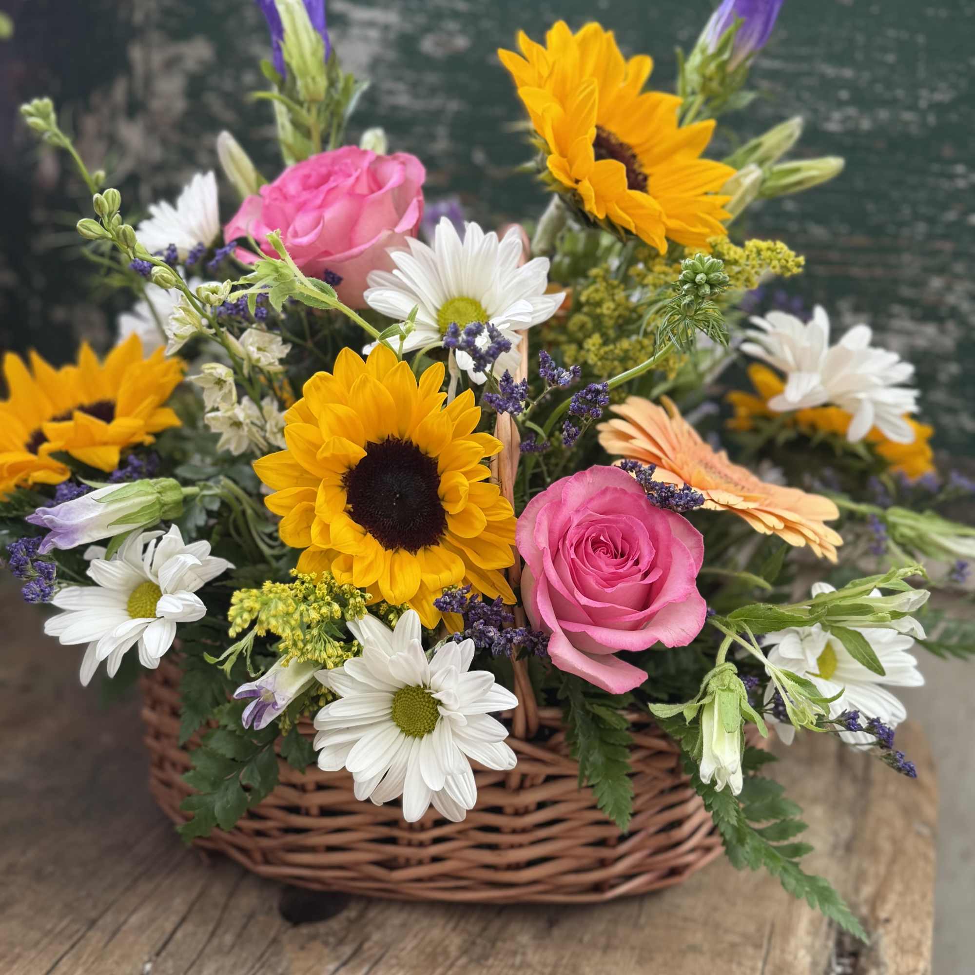 Basket arrangement with pink roses, sunflowers, and white daisies