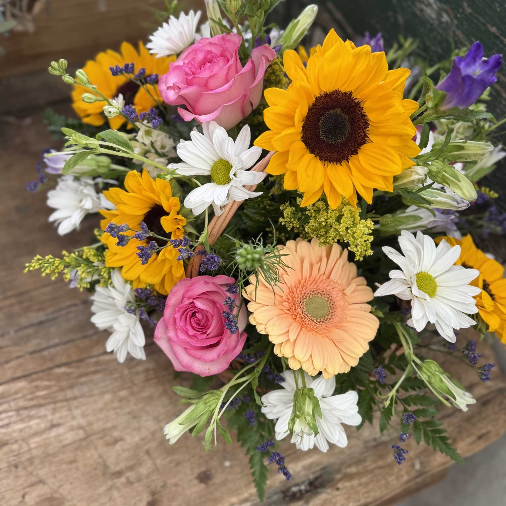 Mixed bouquet with pink roses, sunflowers, daisies, and purple blooms