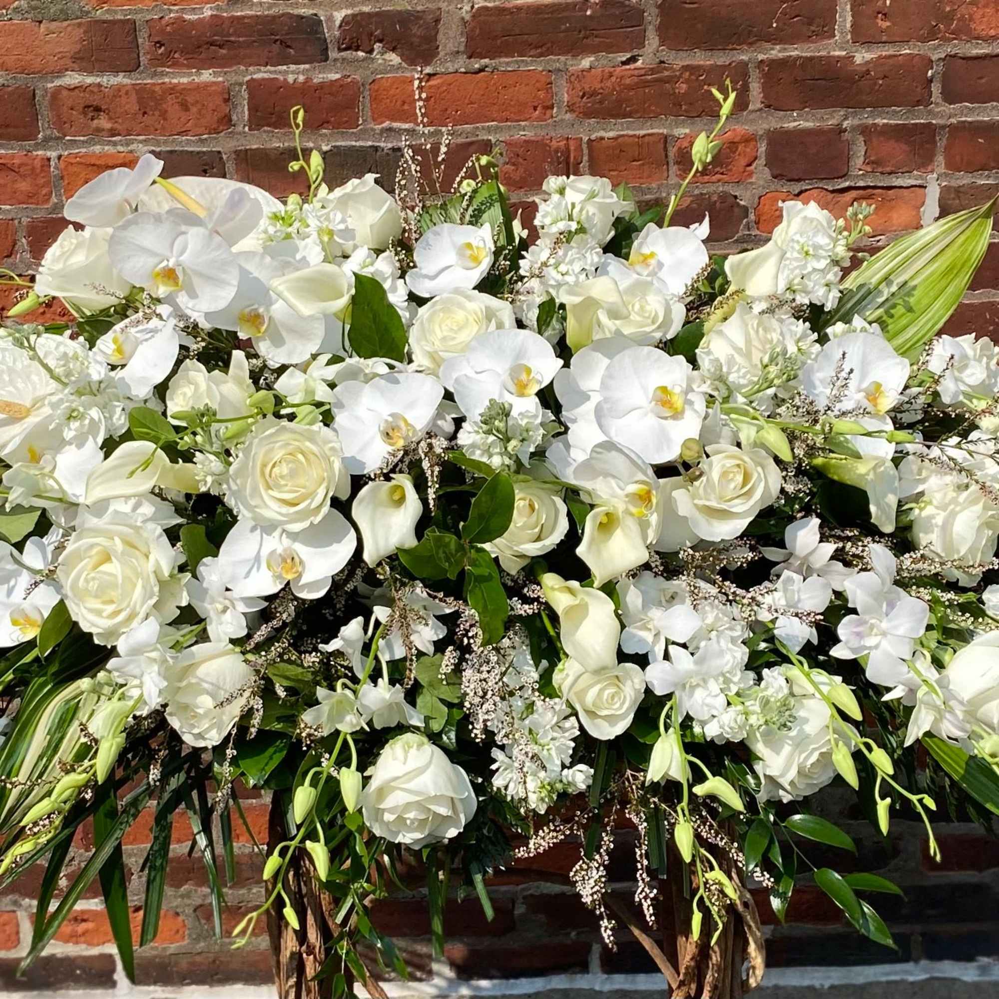 Large white floral spray with orchids and roses against a brick wall