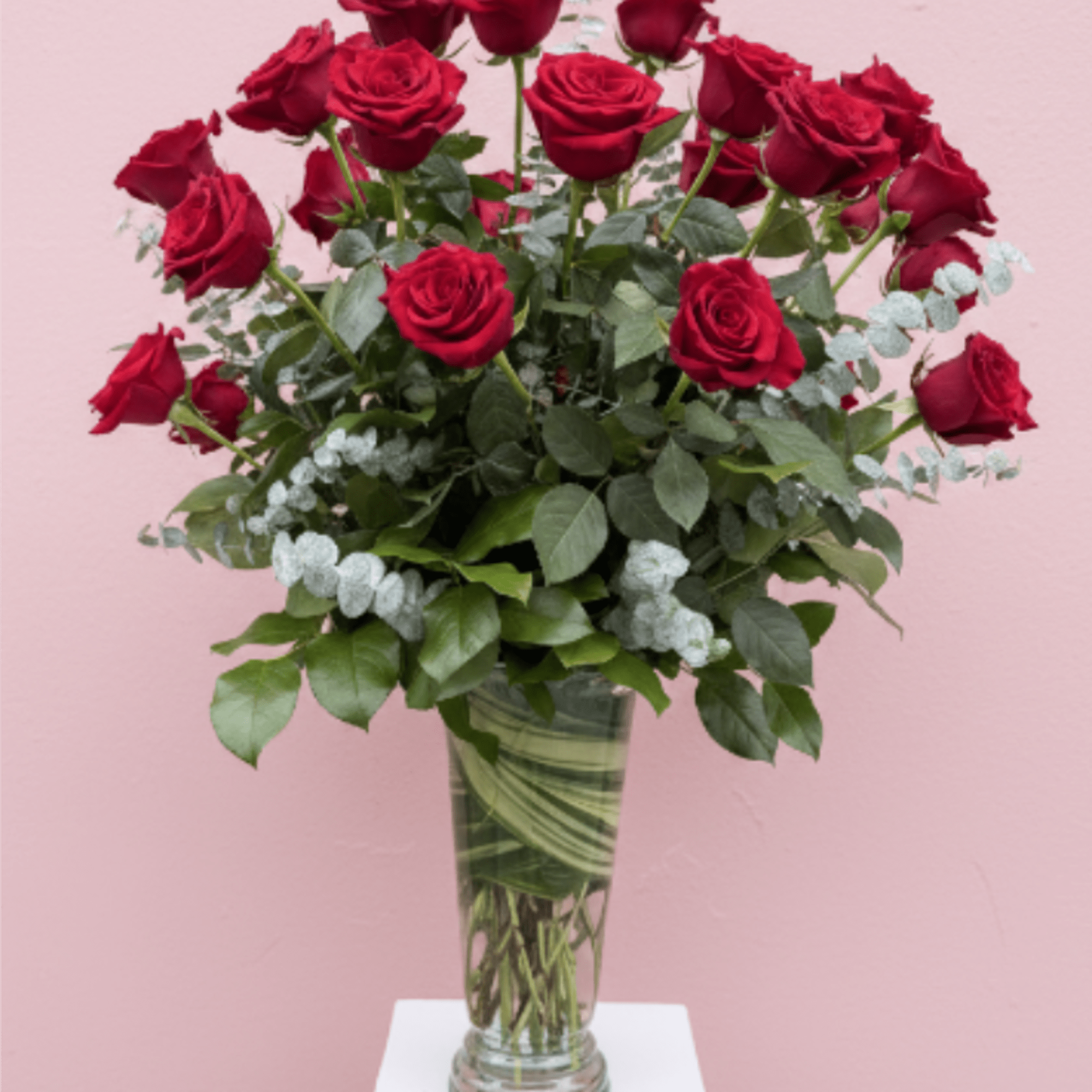 Tall vase arrangement of red roses with greenery