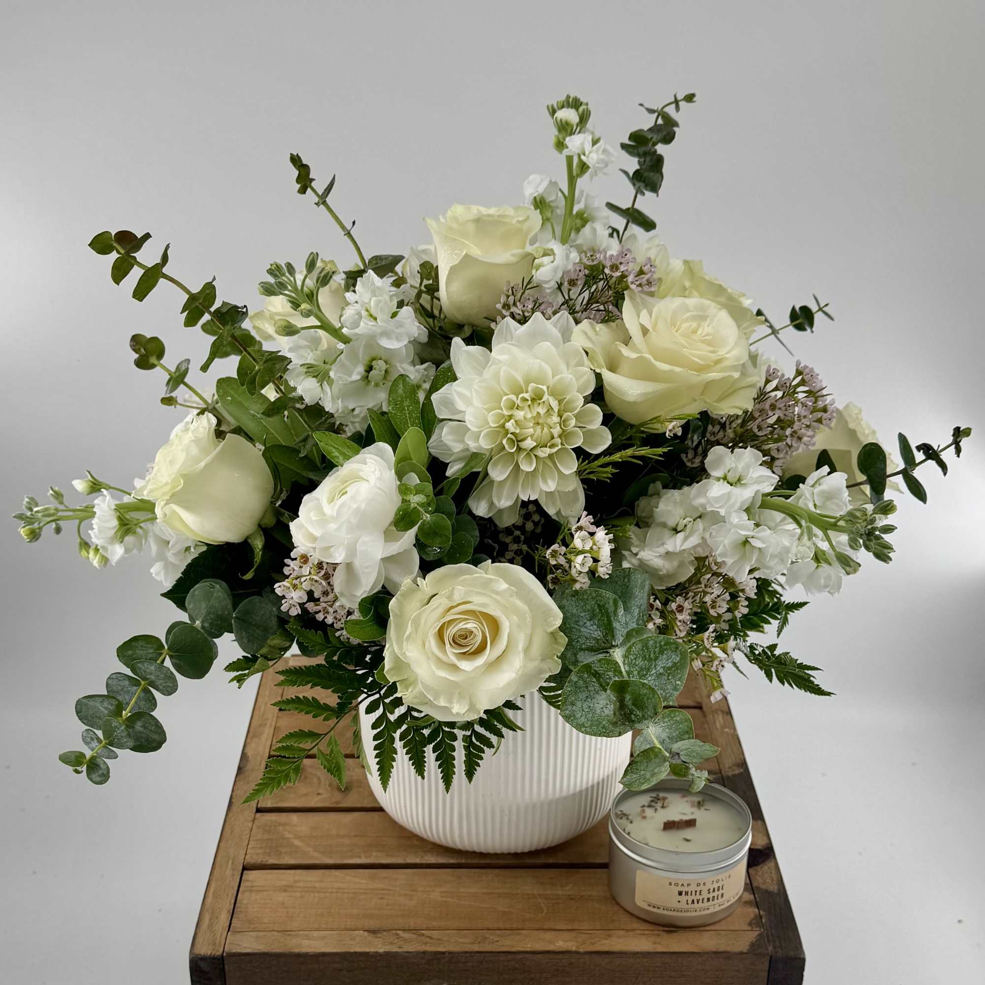 White rose arrangement in a ribbed vase with a small candle beside it