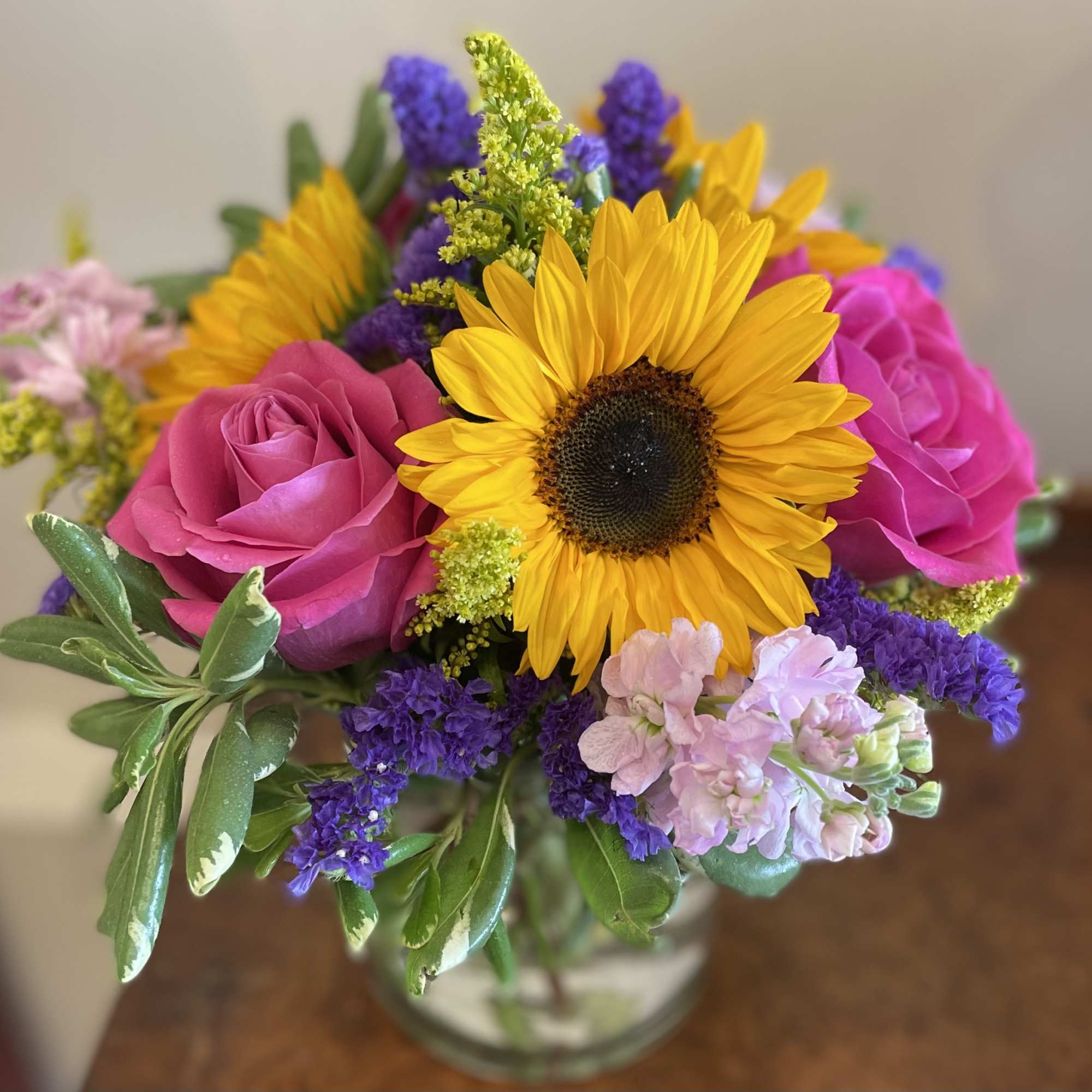 Bouquet of sunflowers, pink roses, and purple filler flowers in a glass vase