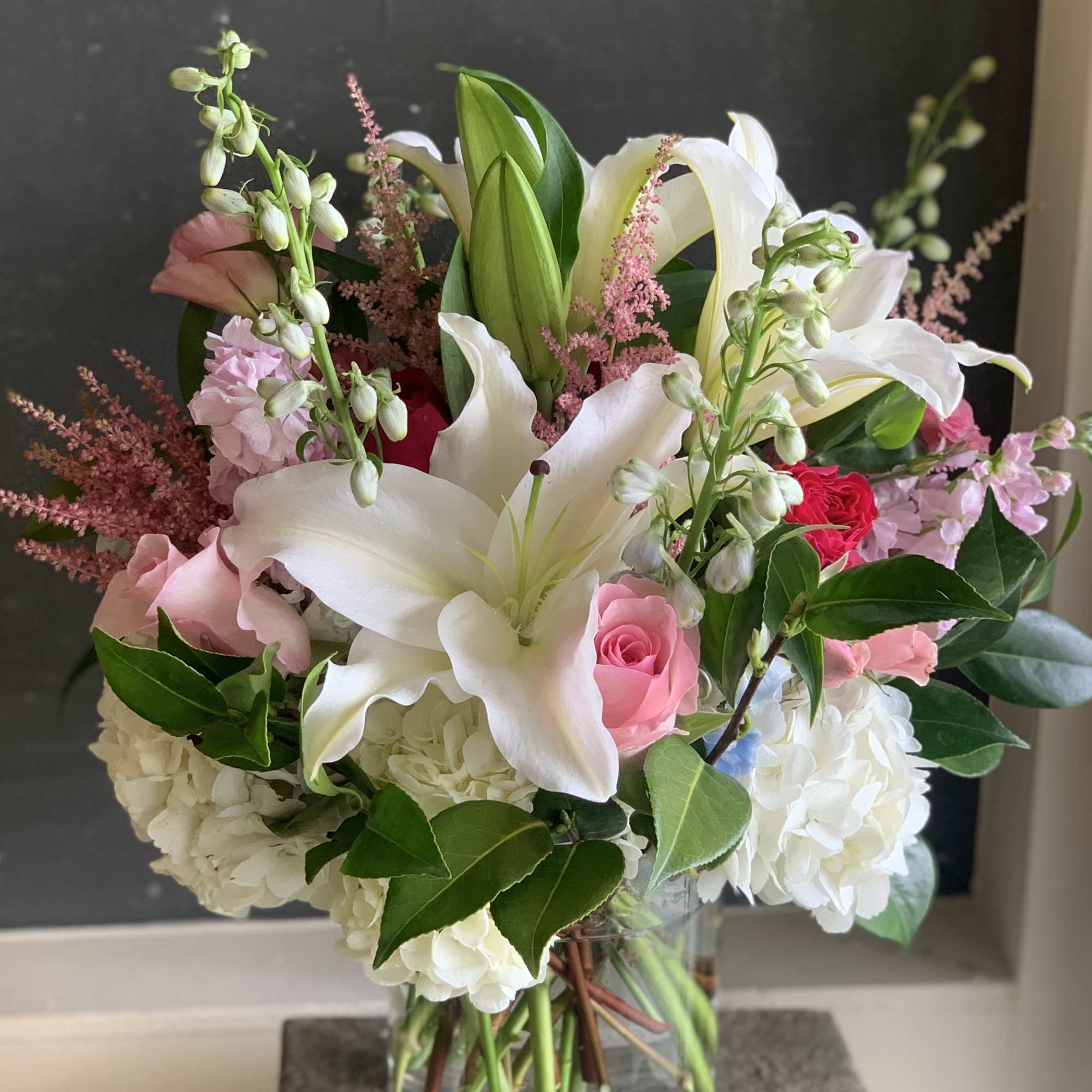 Bouquet of white lilies, pink roses, and white hydrangeas in a glass vase.