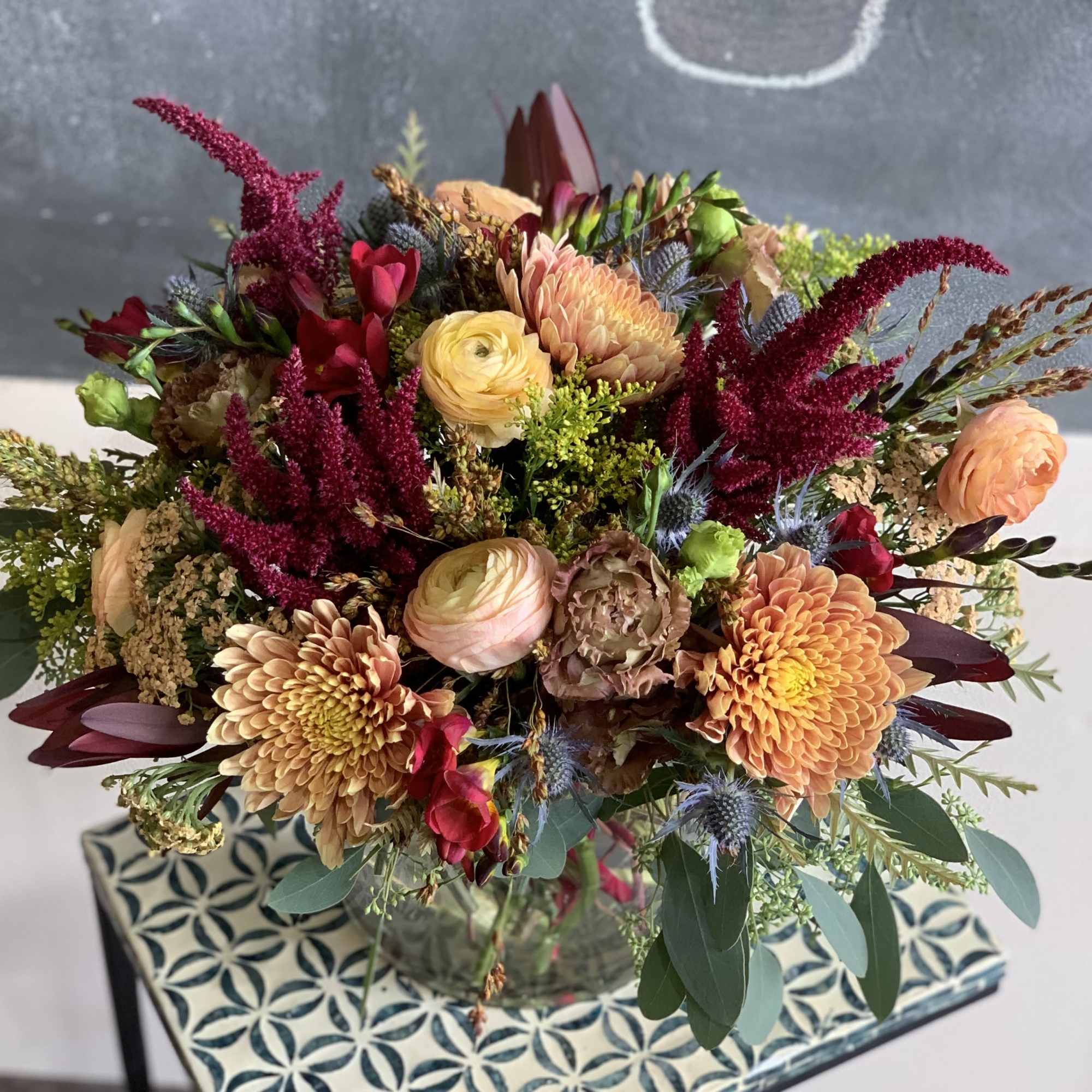 Mixed bouquet of peach, yellow, and burgundy flowers in a glass vase