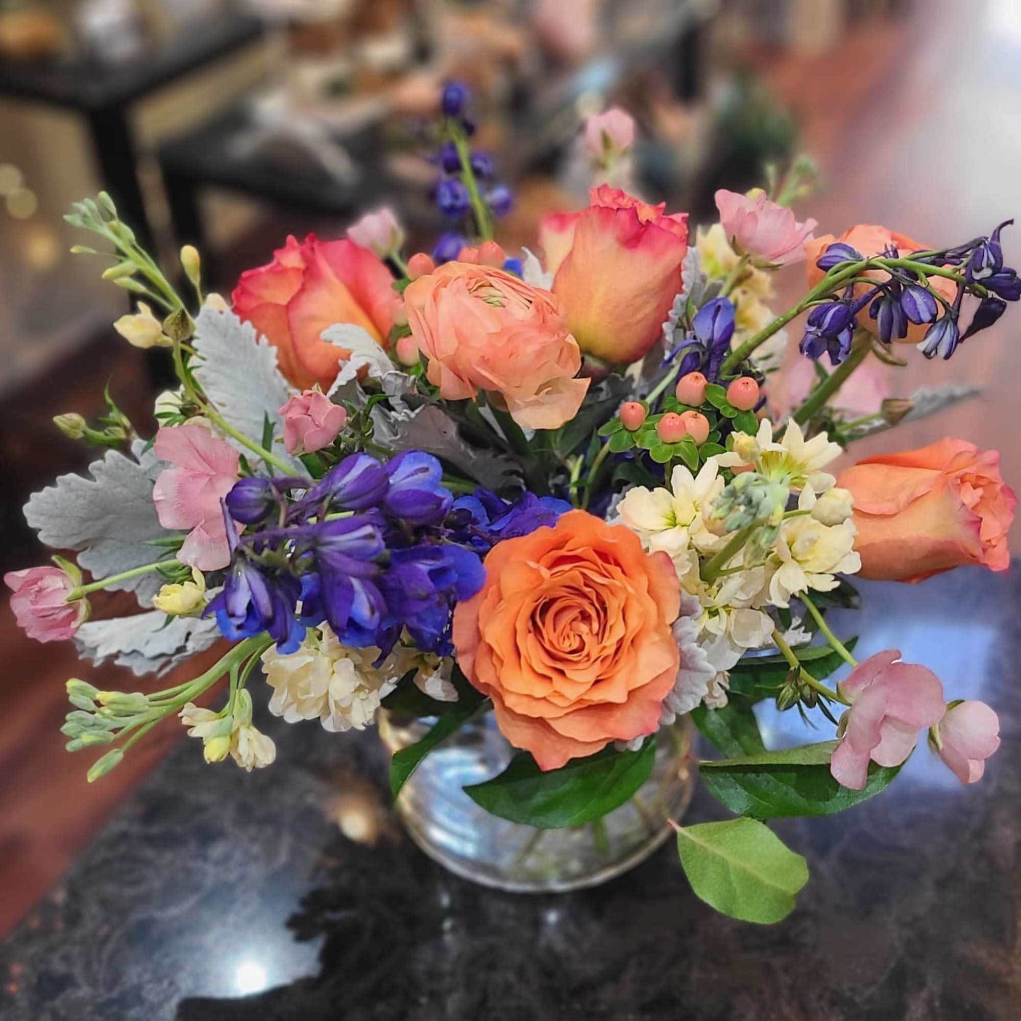 Mixed bouquet of orange roses and blue flowers in a glass vase