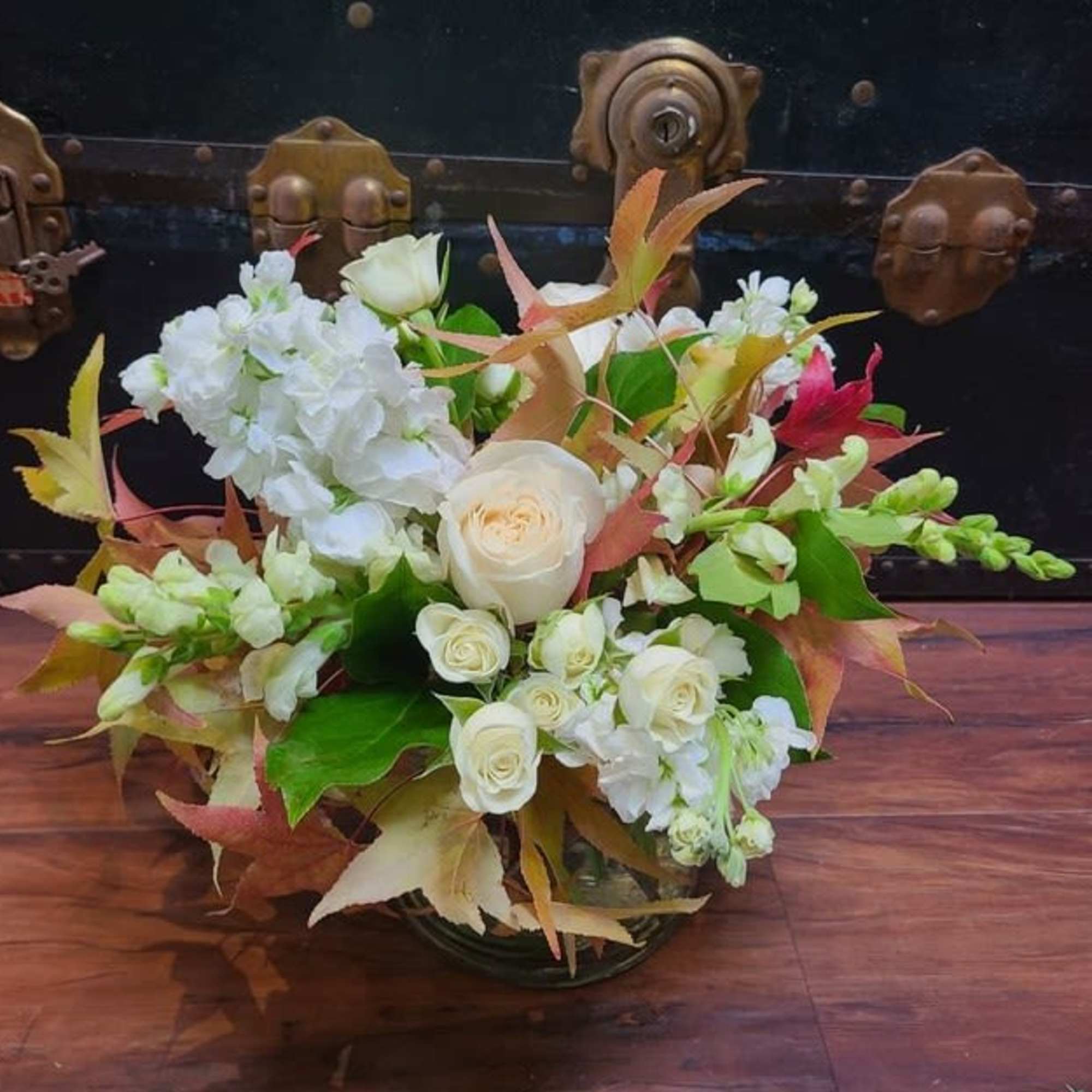 White roses and hydrangeas arranged in a glass bowl with autumn leaves