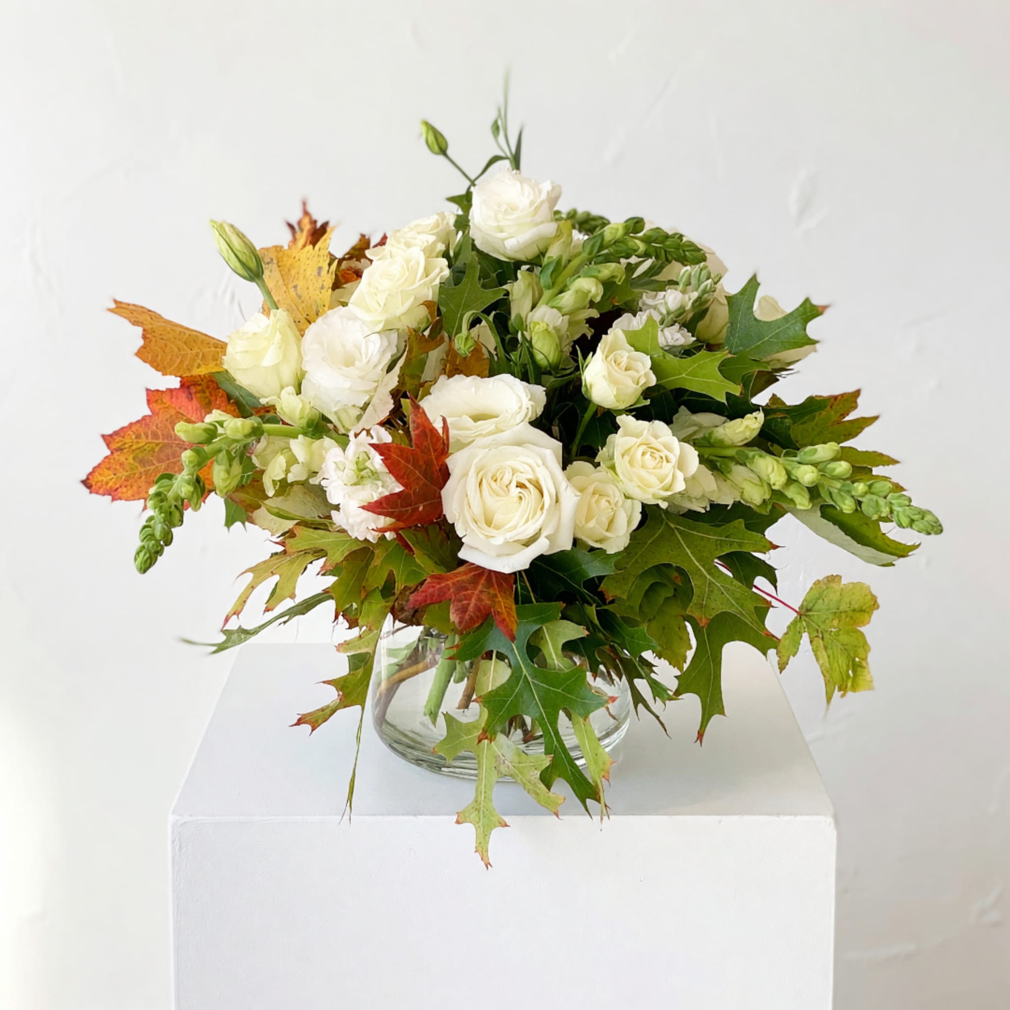 White rose bouquet in a clear glass vase with autumn leaves