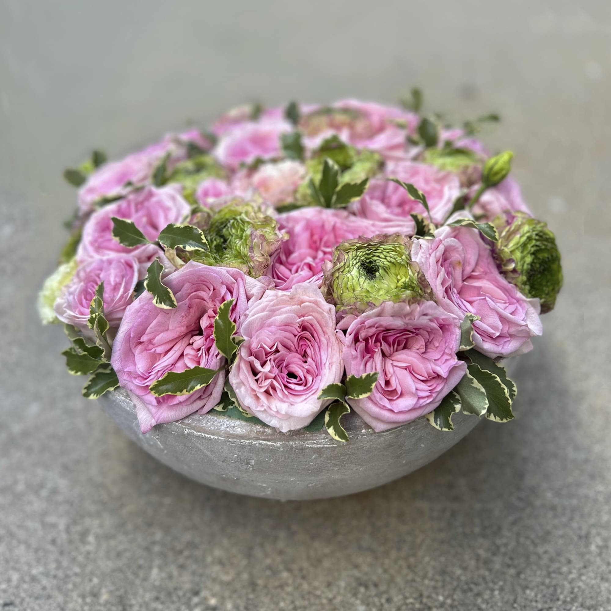 Pink roses arranged in a low gray bowl with variegated foliage