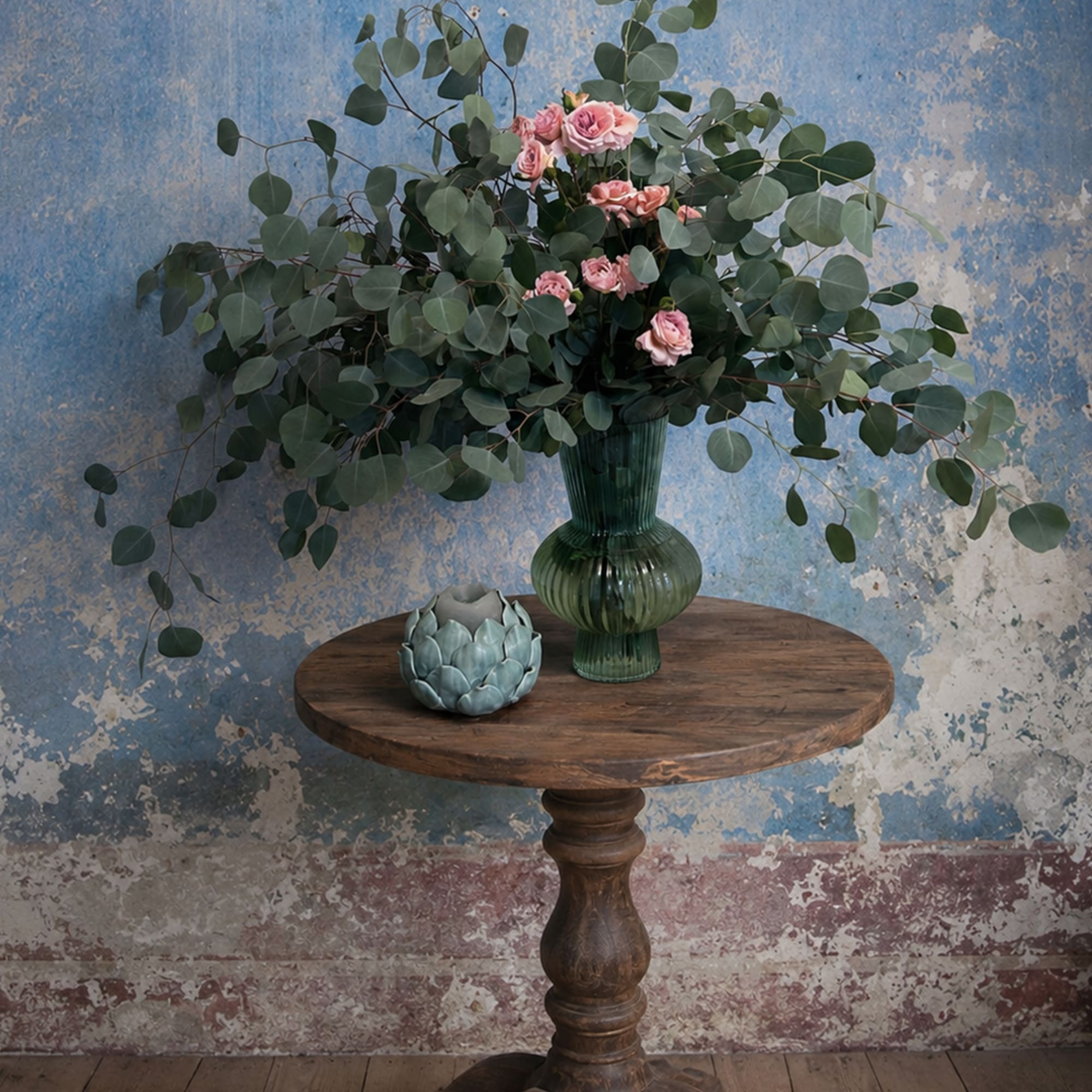 Pink roses in a green glass vase with eucalyptus on a wooden table