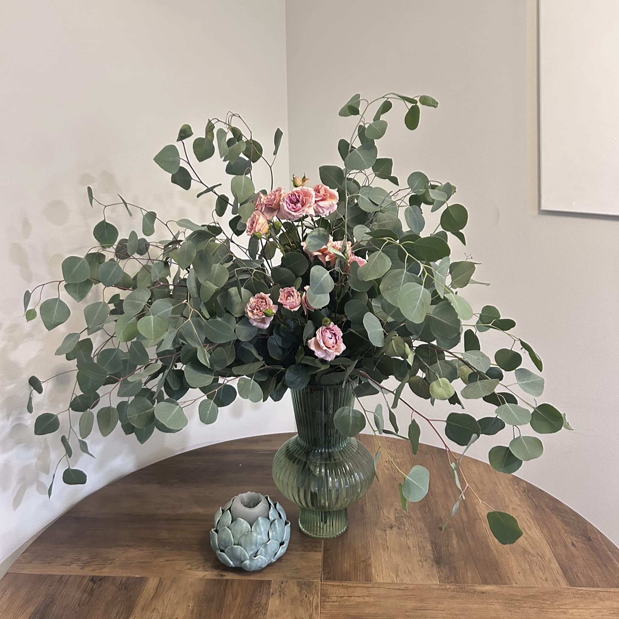 Pink spray roses in a green glass vase with large eucalyptus branches