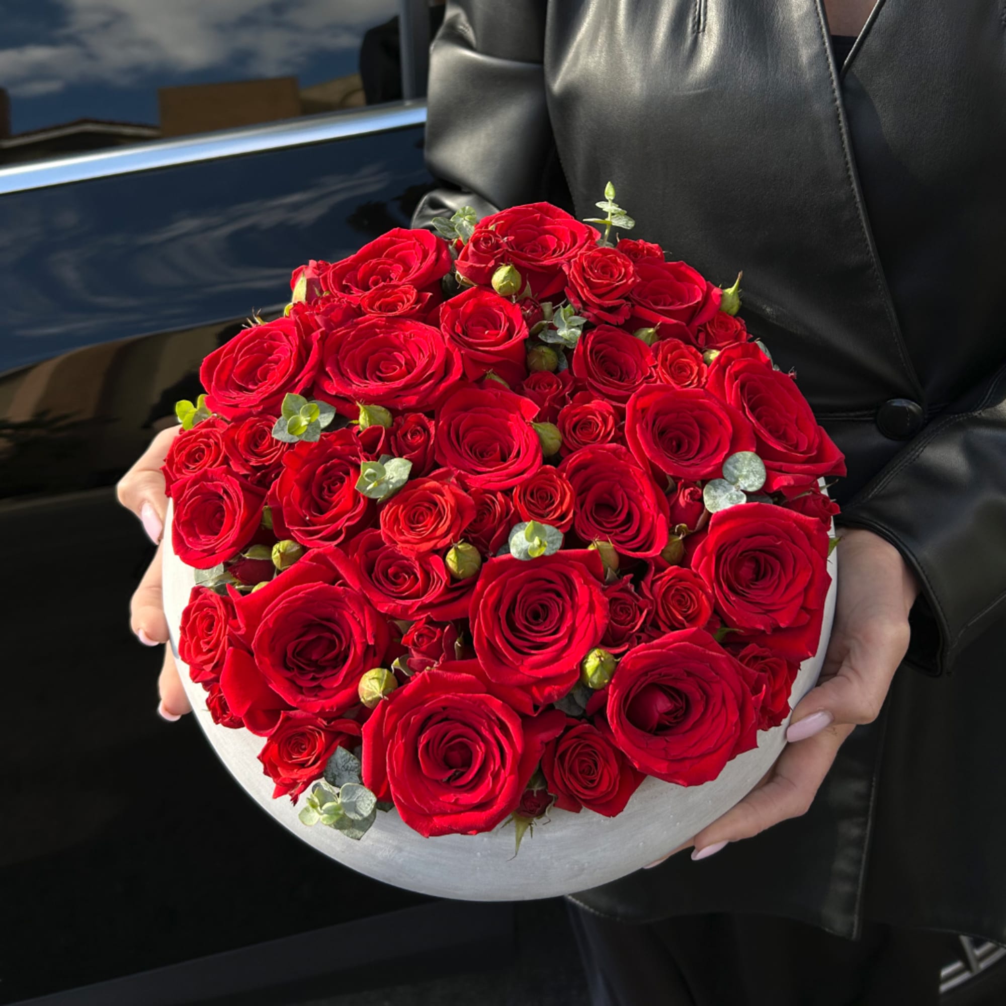 Round bouquet of red roses in a white box, held by a person
