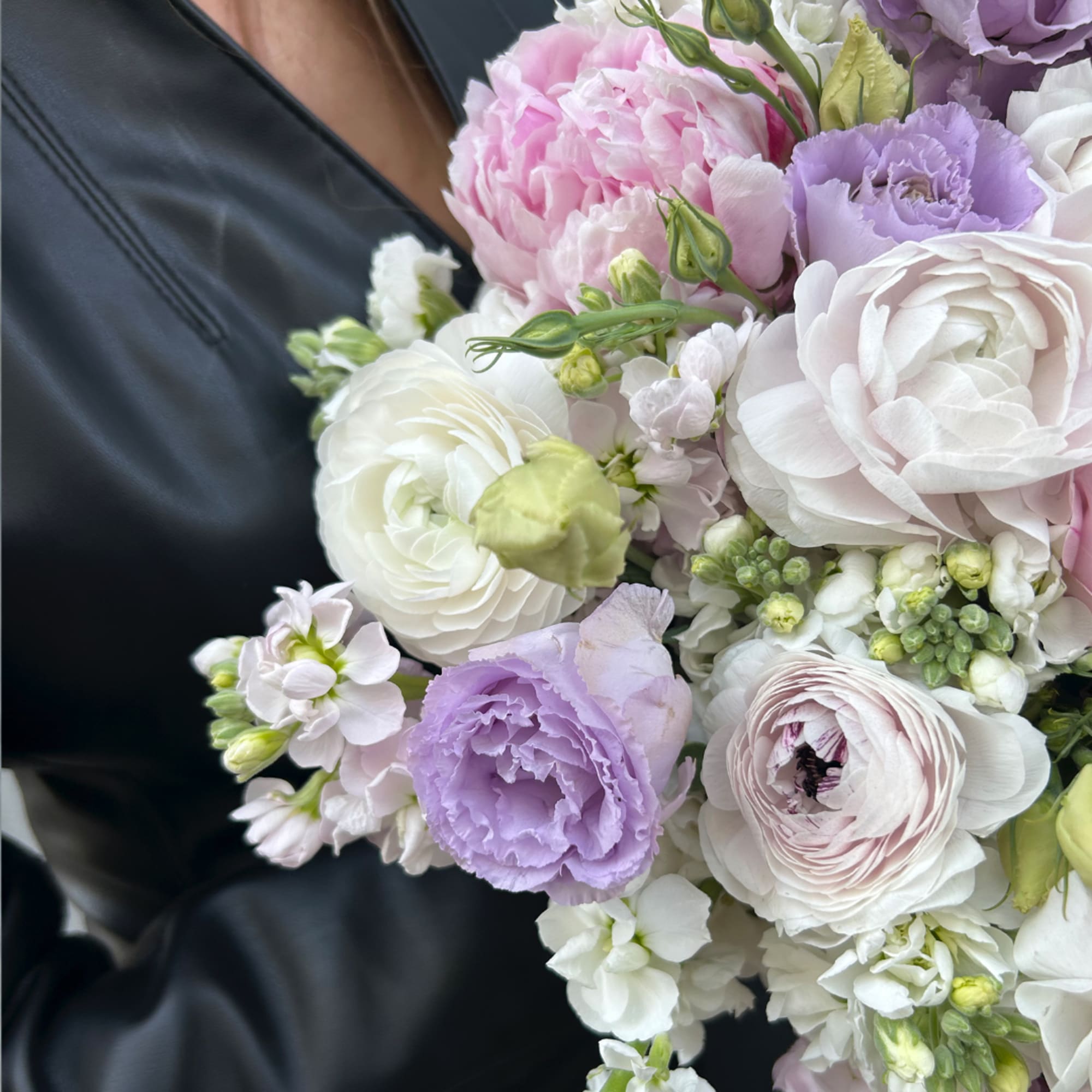 Bouquet of pink, white, and lavender flowers held against a dark jacket