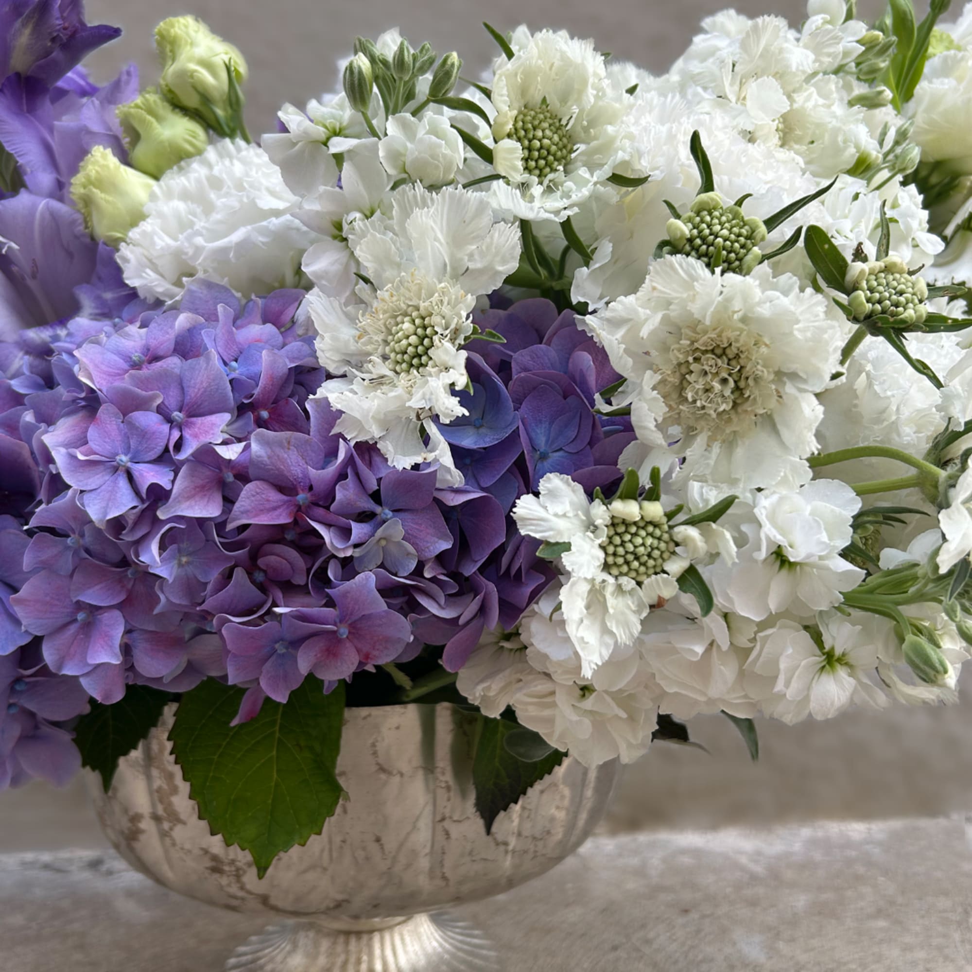 Purple and white floral arrangement in a decorative bowl vase
