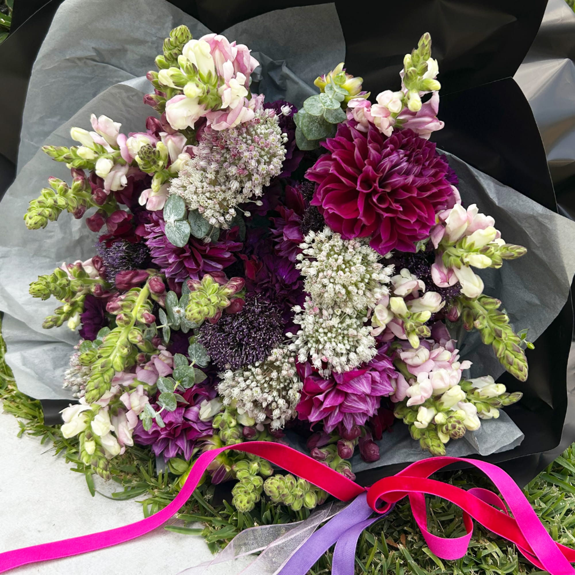 Bouquet of purple and white flowers wrapped in dark paper with pink and purple ribbon