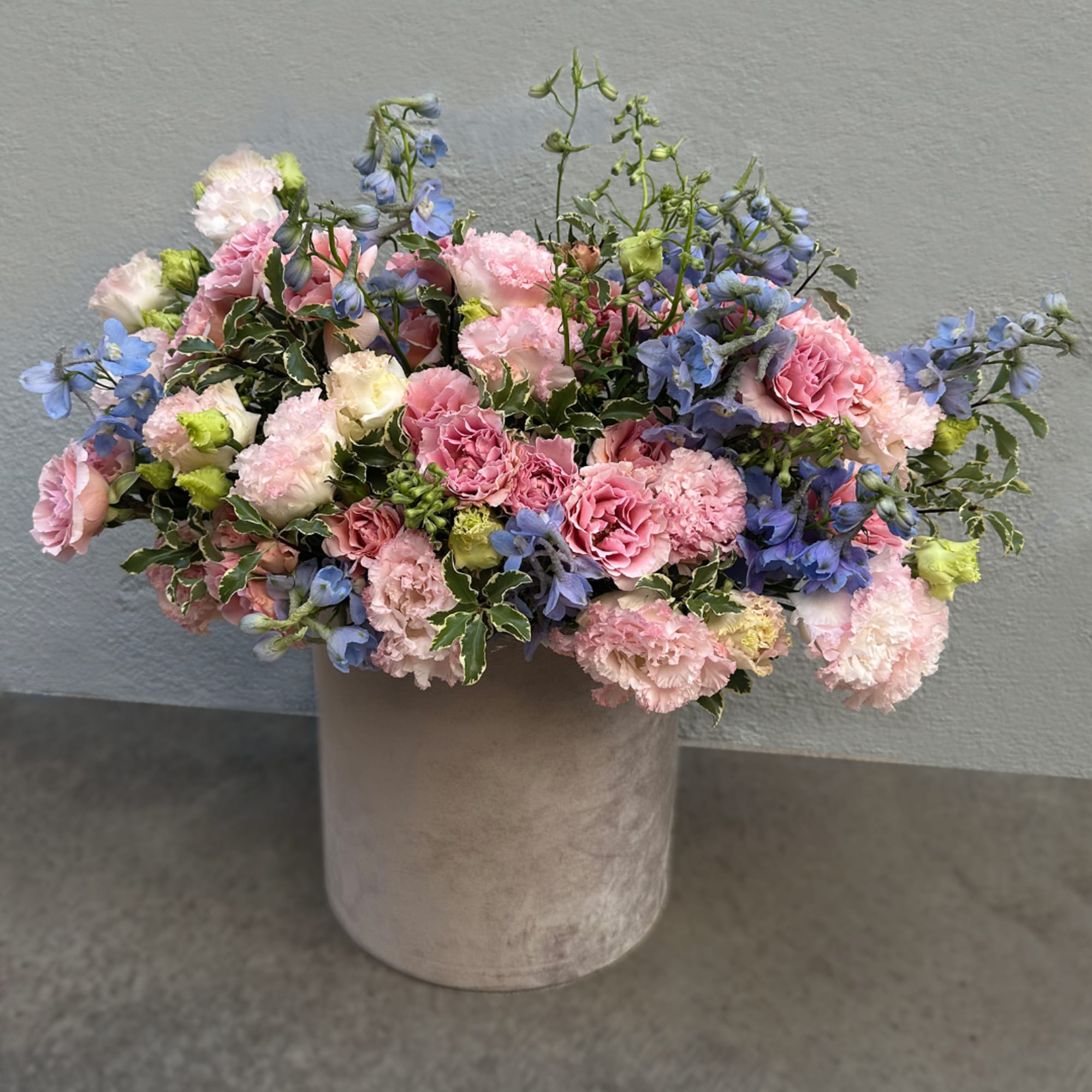 Pink and blue mixed flower arrangement in a beige vase