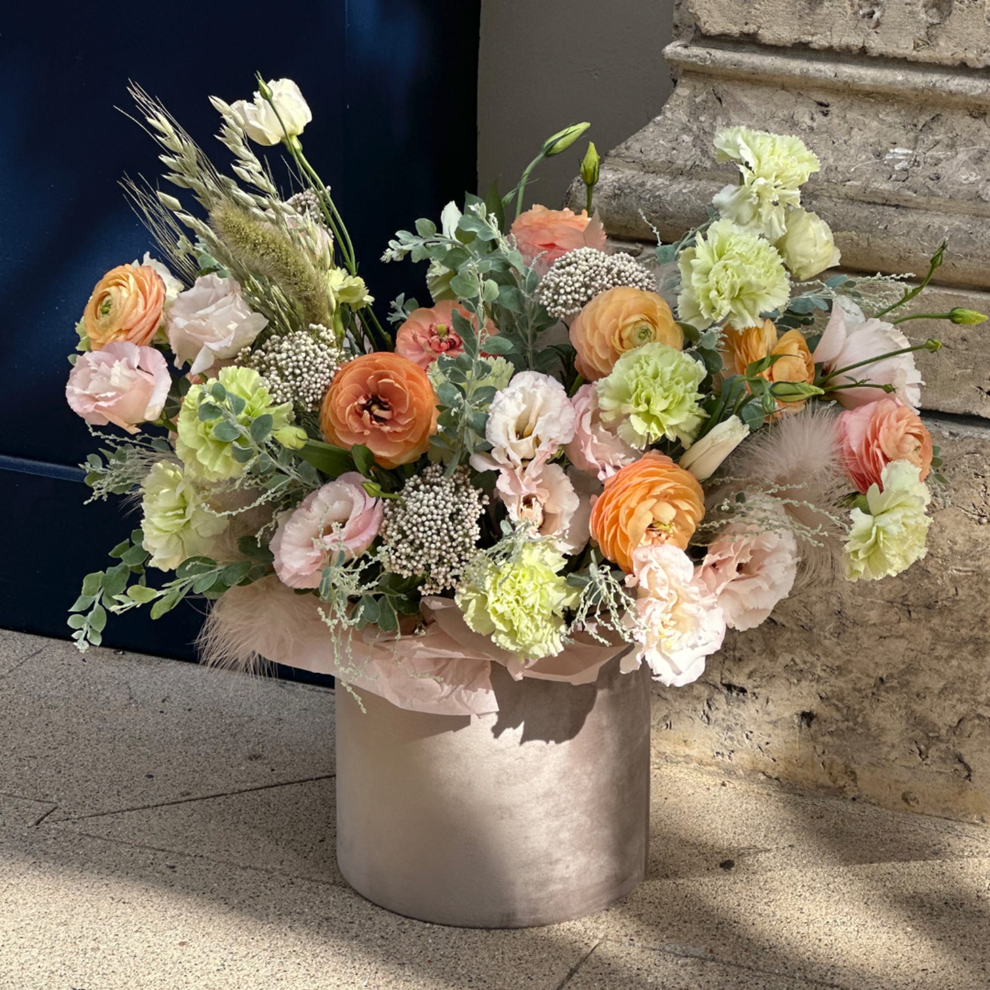 Pastel floral arrangement in a round silver vase with peach, pink, and green blooms