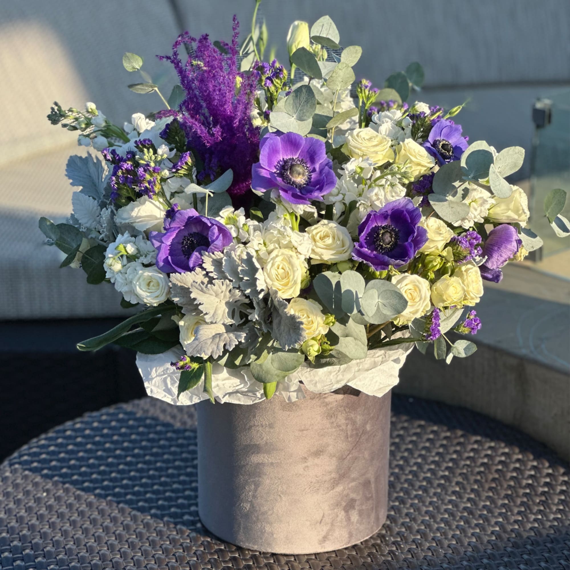 Purple anemones and white roses in a gray hatbox vase