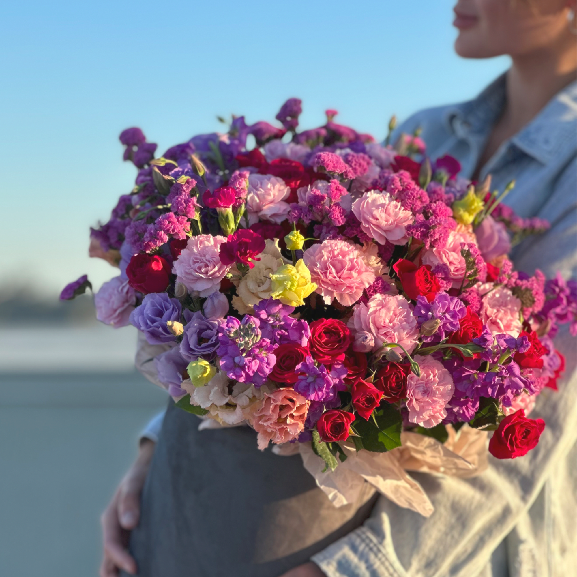 Person holding a large bouquet of pink, purple, and red flowers