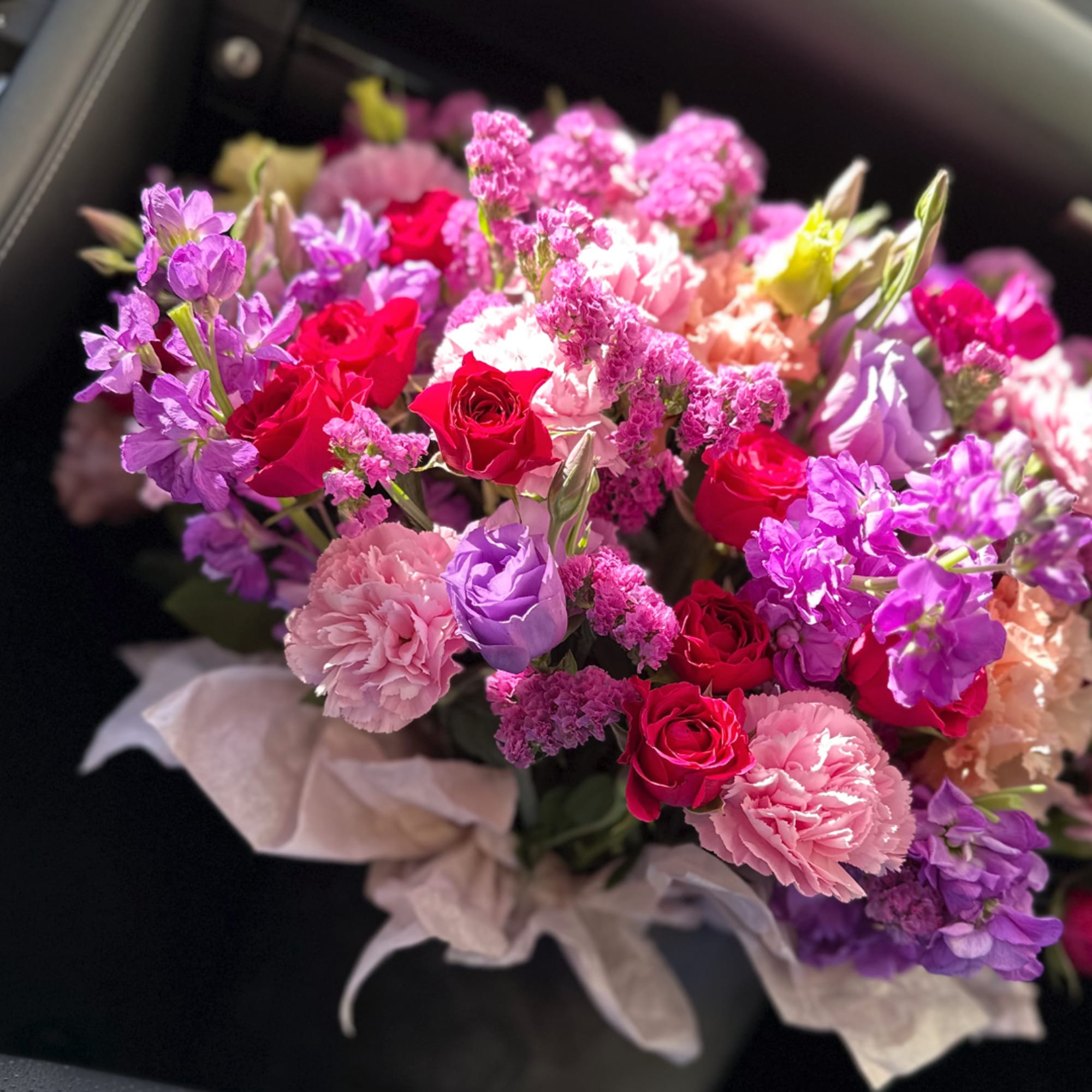 Bouquet of pink, purple, and red flowers wrapped in pale paper