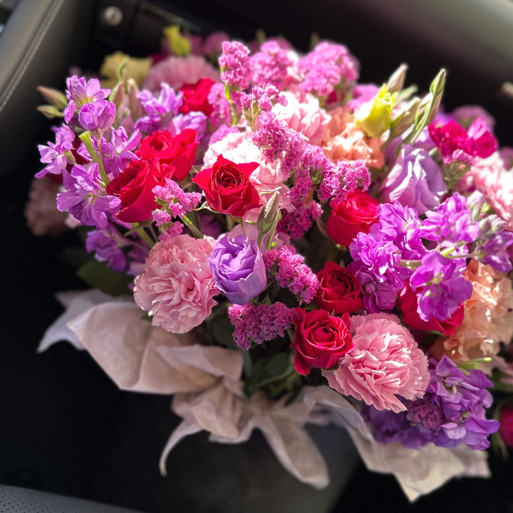 Bouquet of pink, purple, and red flowers wrapped in pale paper