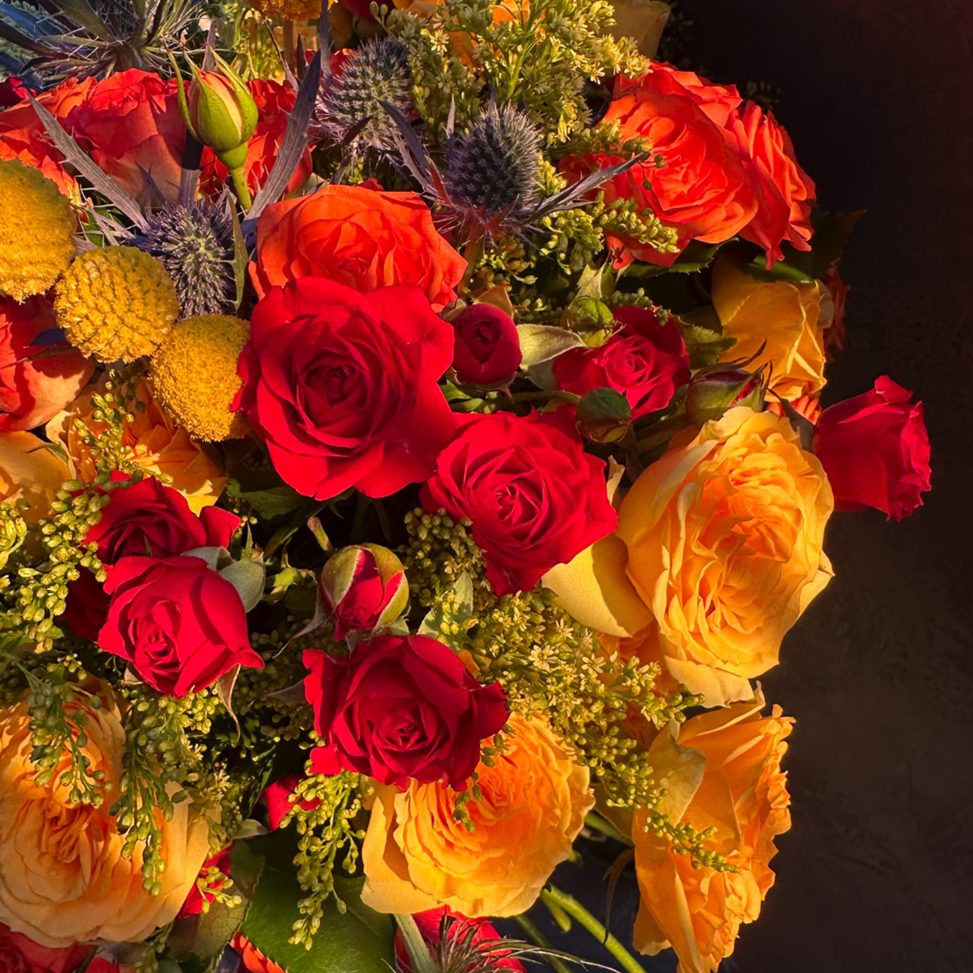 Bouquet of red and yellow roses with thistle-like blue accents