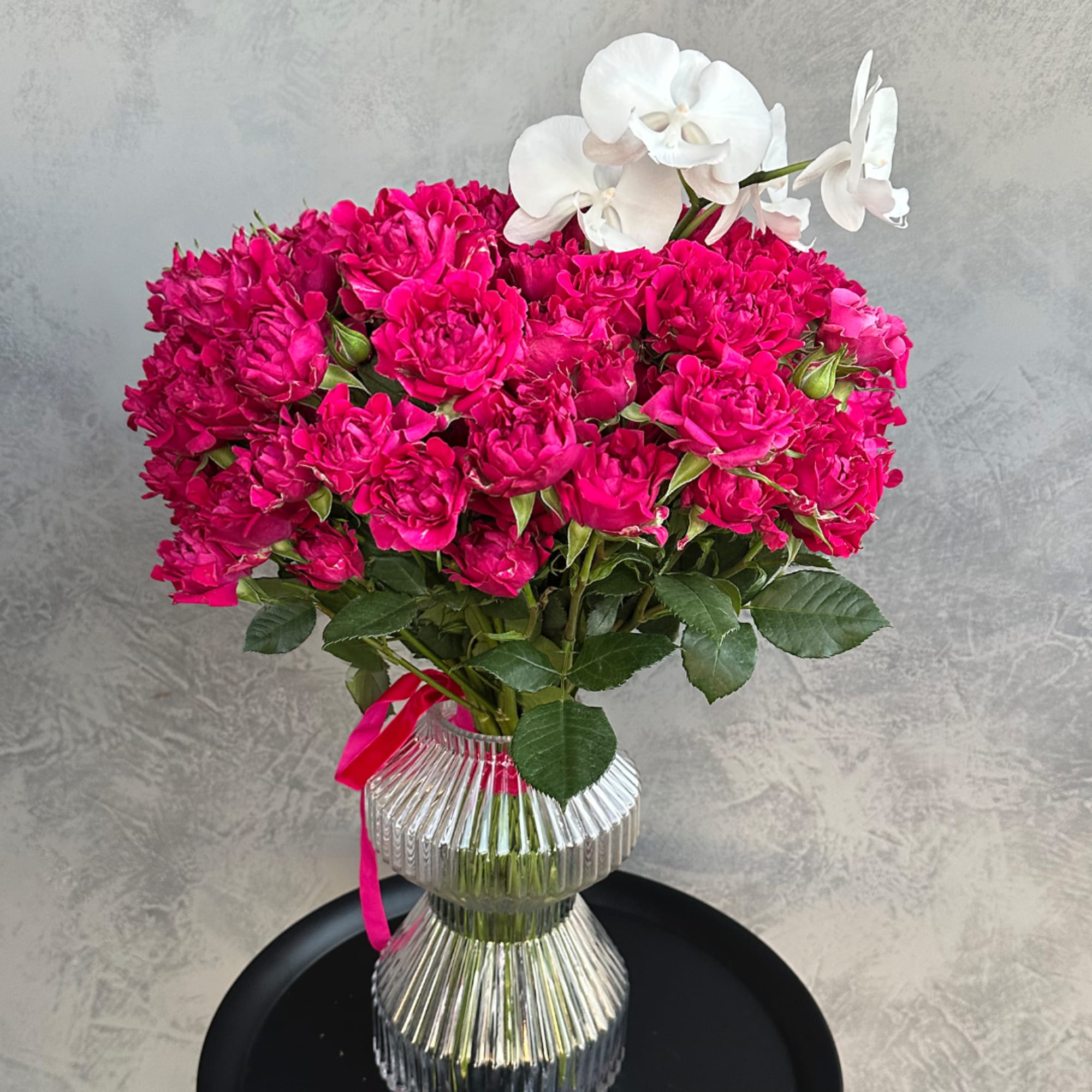 Hot pink roses in a ribbed glass vase with white orchids