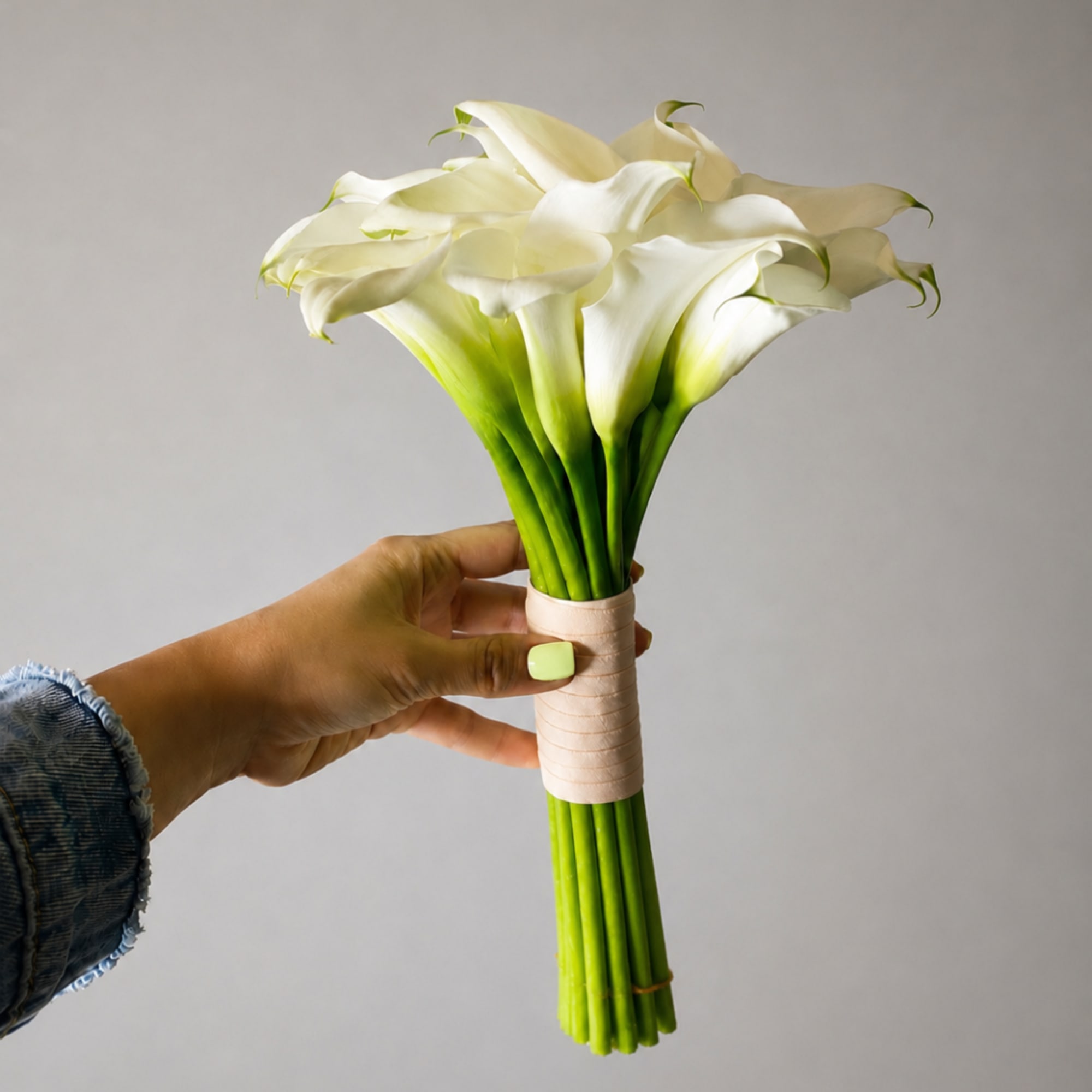 Hand holding a bouquet of white calla lilies with wrapped stems