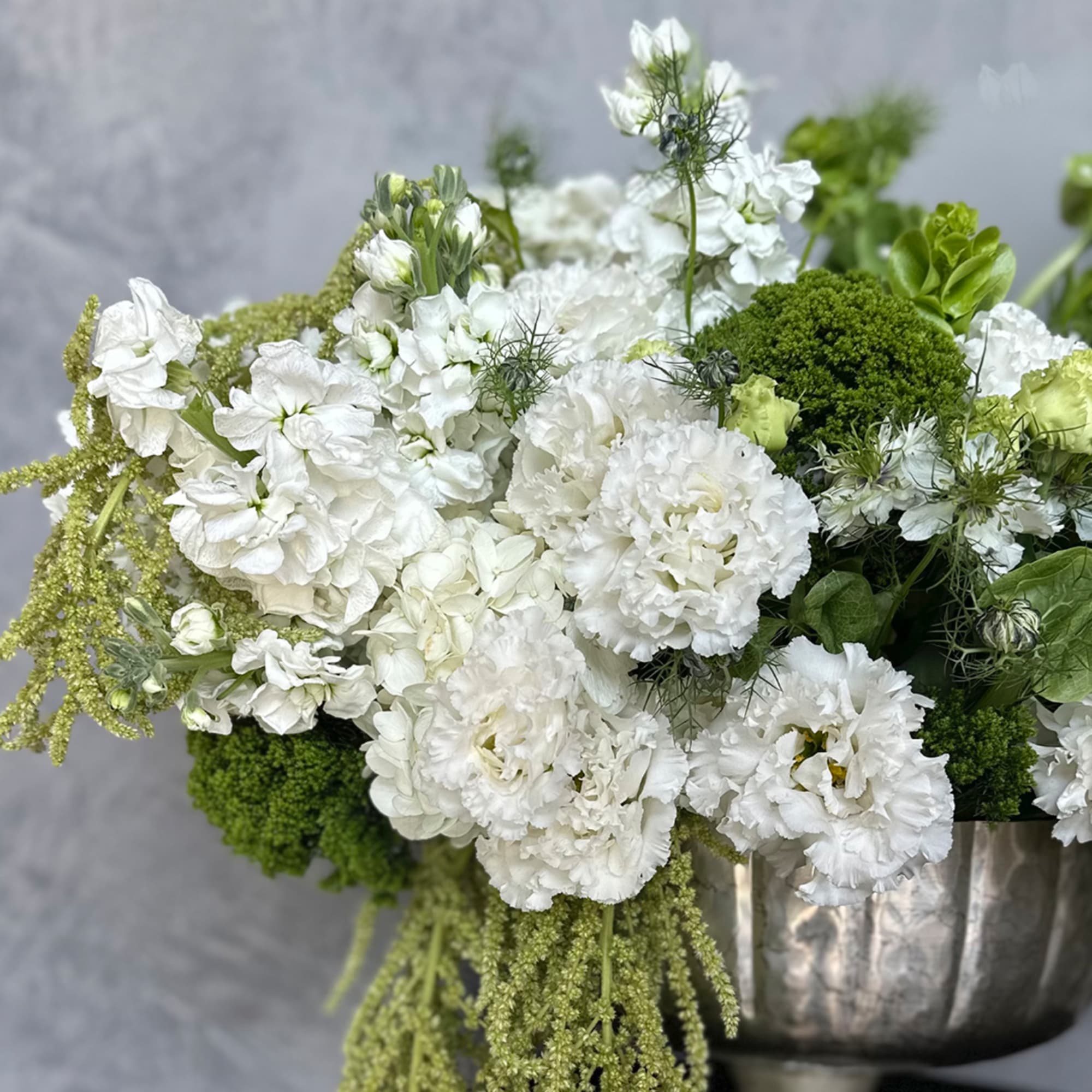 White flowers arranged in a silver vase with green accents