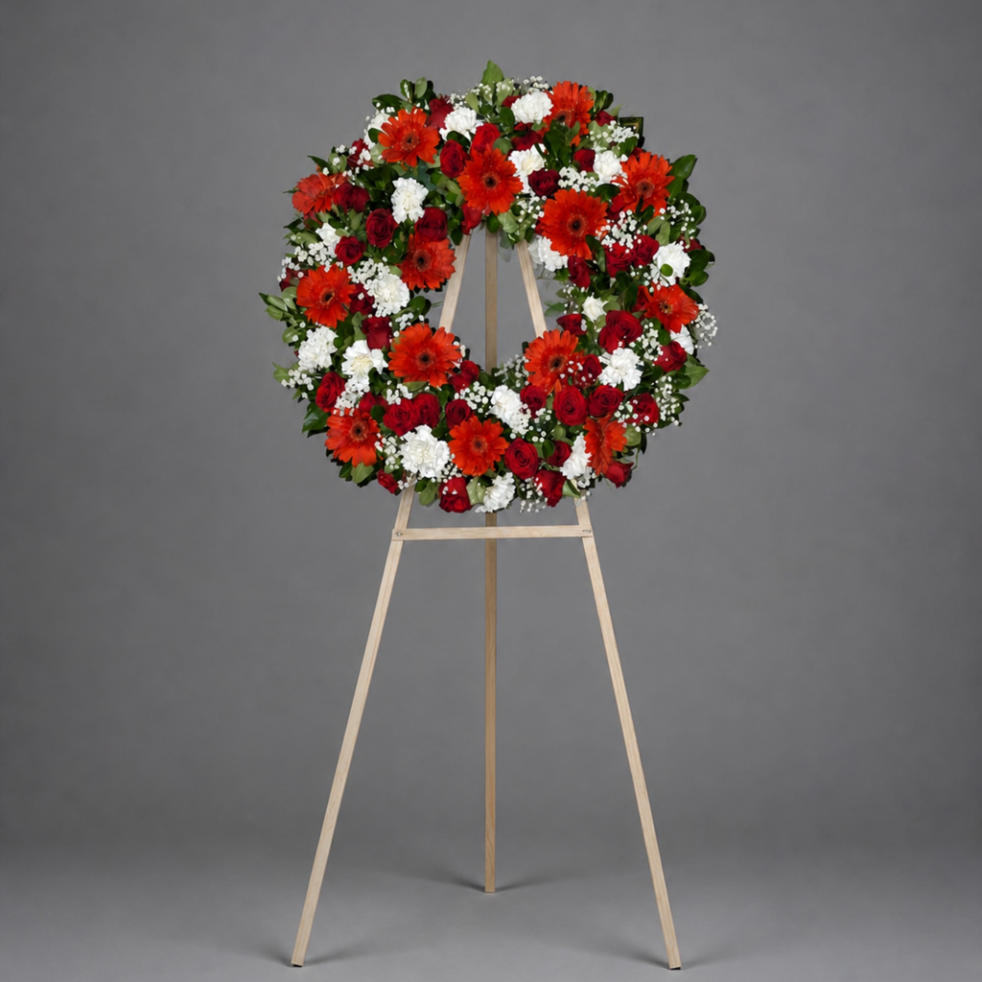 Circular wreath of red, white, and orange flowers on a wooden easel