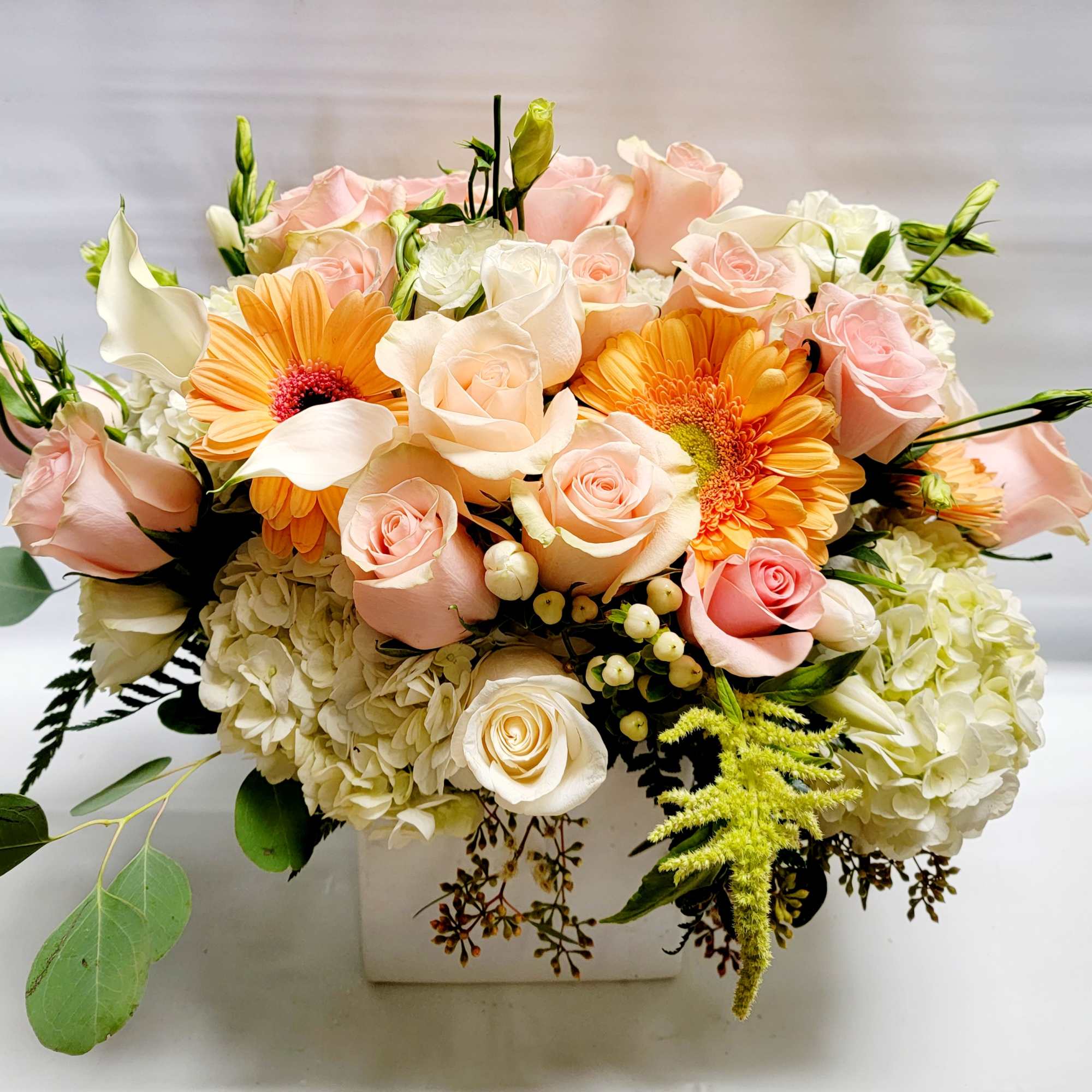 Peach roses and orange gerbera daisies in a white square vase