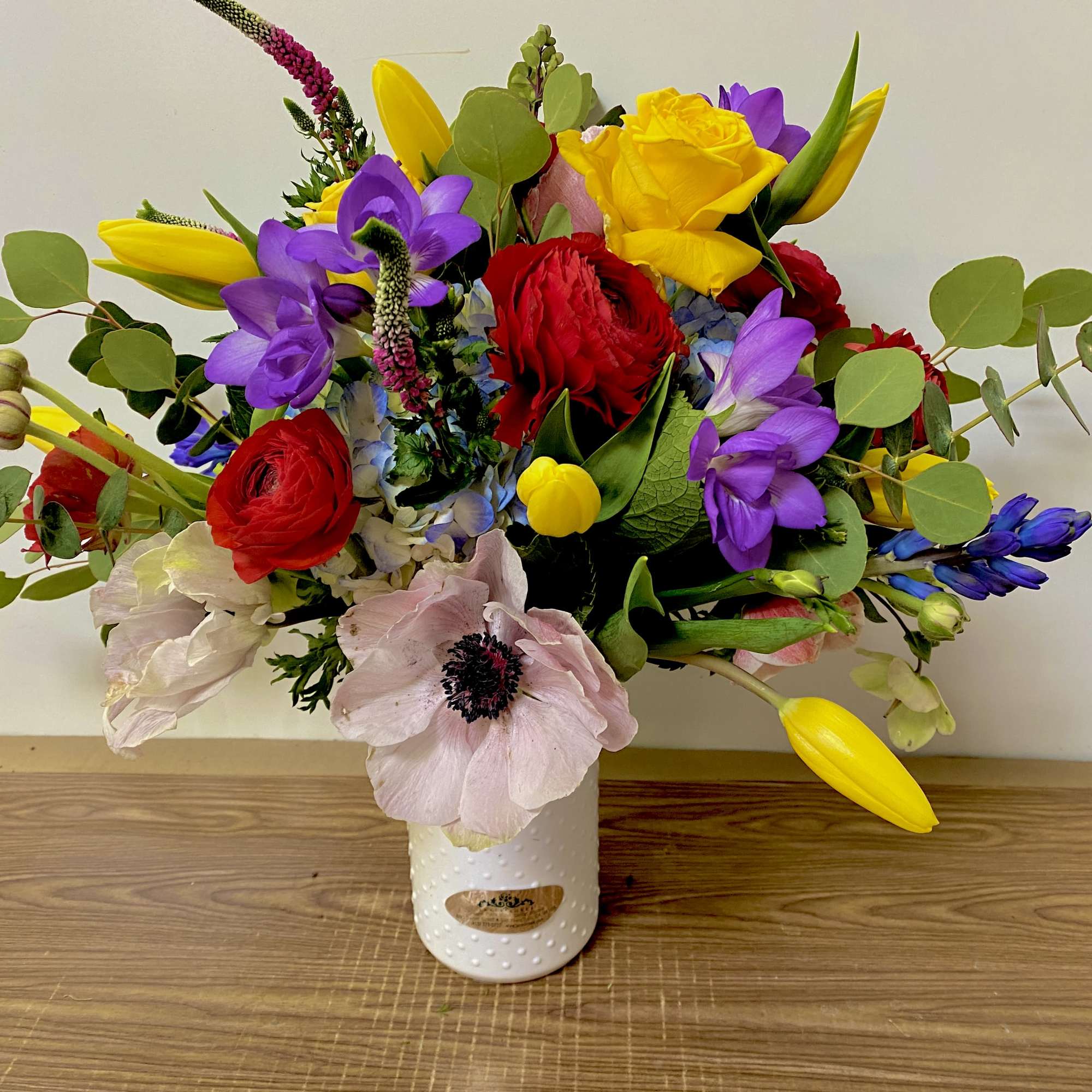 Colorful mixed bouquet in a white vase with red, yellow, purple, and pale pink blooms