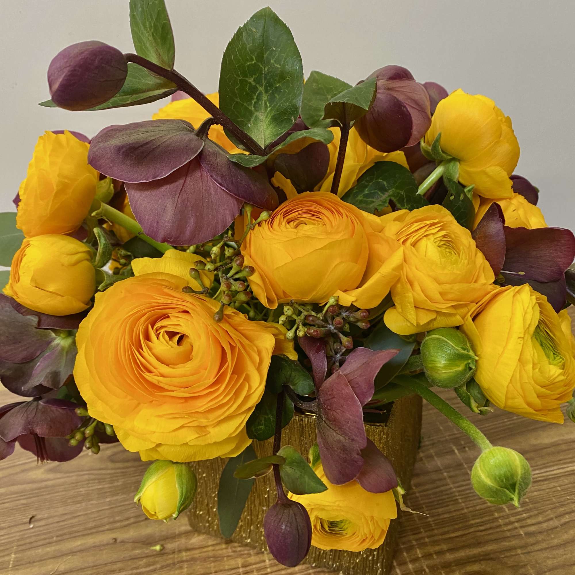 Yellow ranunculus bouquet with purple accents in a gold vase