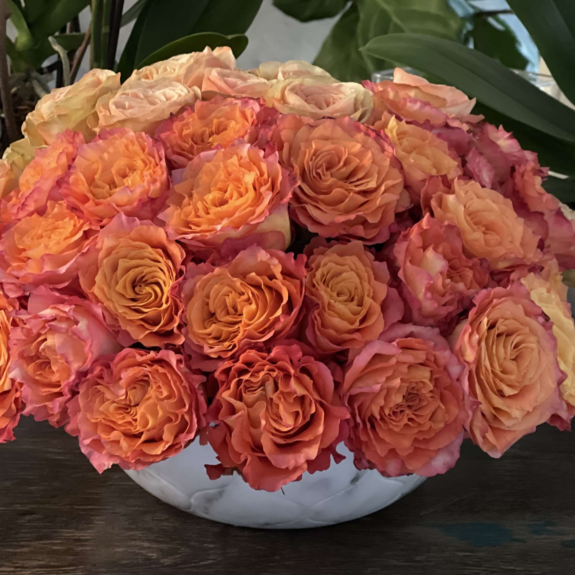 A low bouquet of orange and pink roses in a white vase