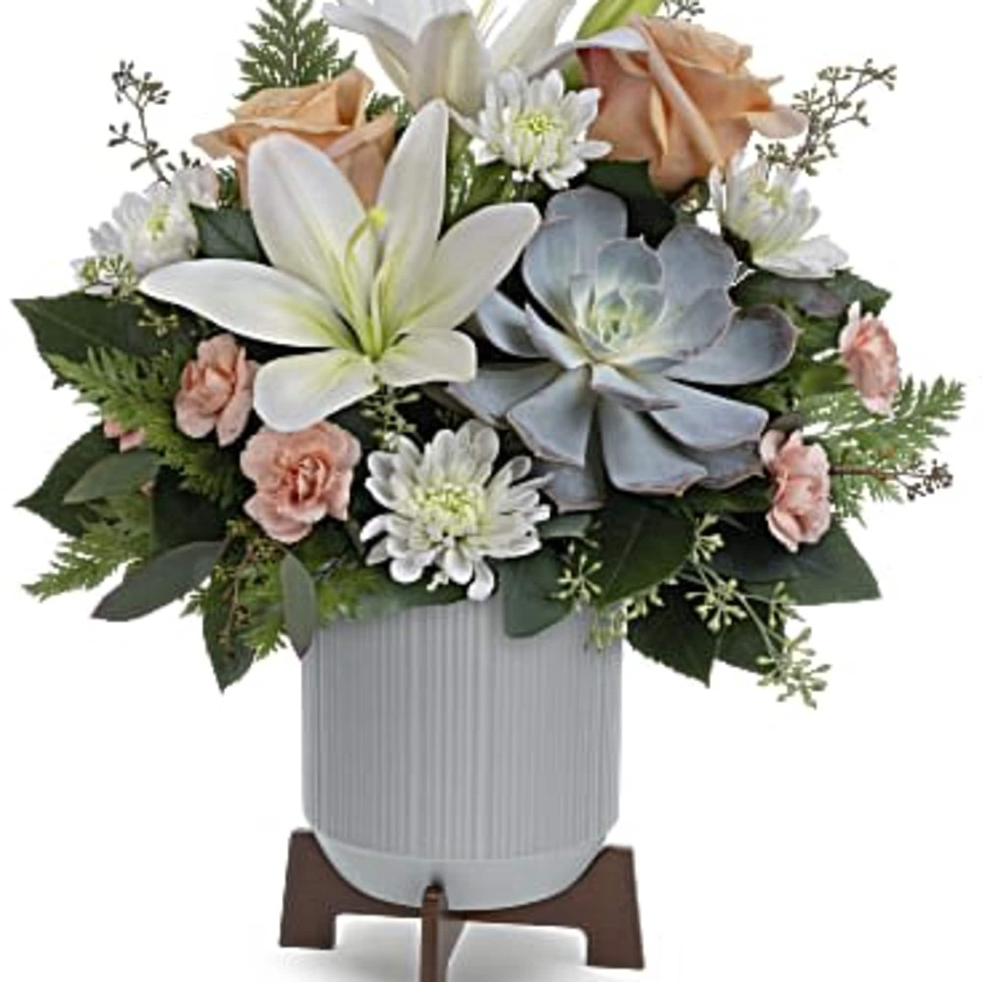 Flower arrangement with white lilies, peach roses, and pale blue succulents in a vase