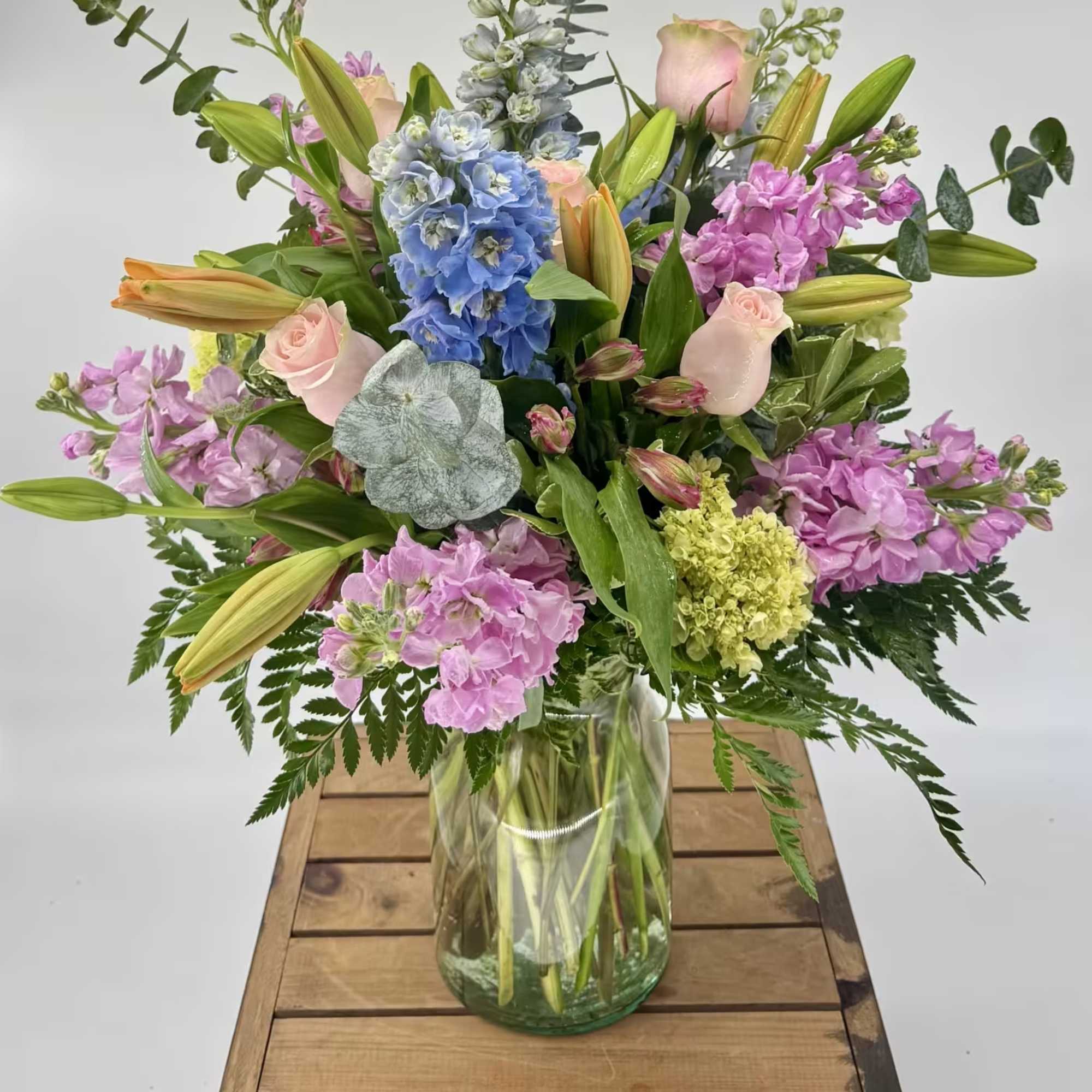 Mixed bouquet of lilies, roses, and blue hydrangea in a glass vase