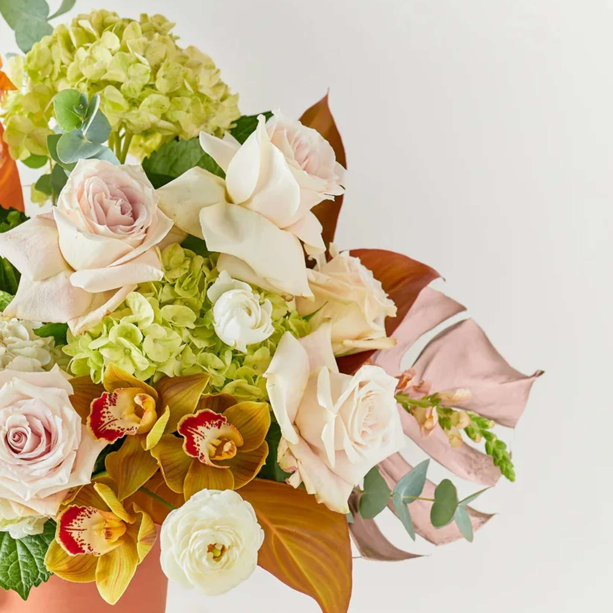 Mixed bouquet of pale roses, hydrangea, and orchids in a terracotta vase