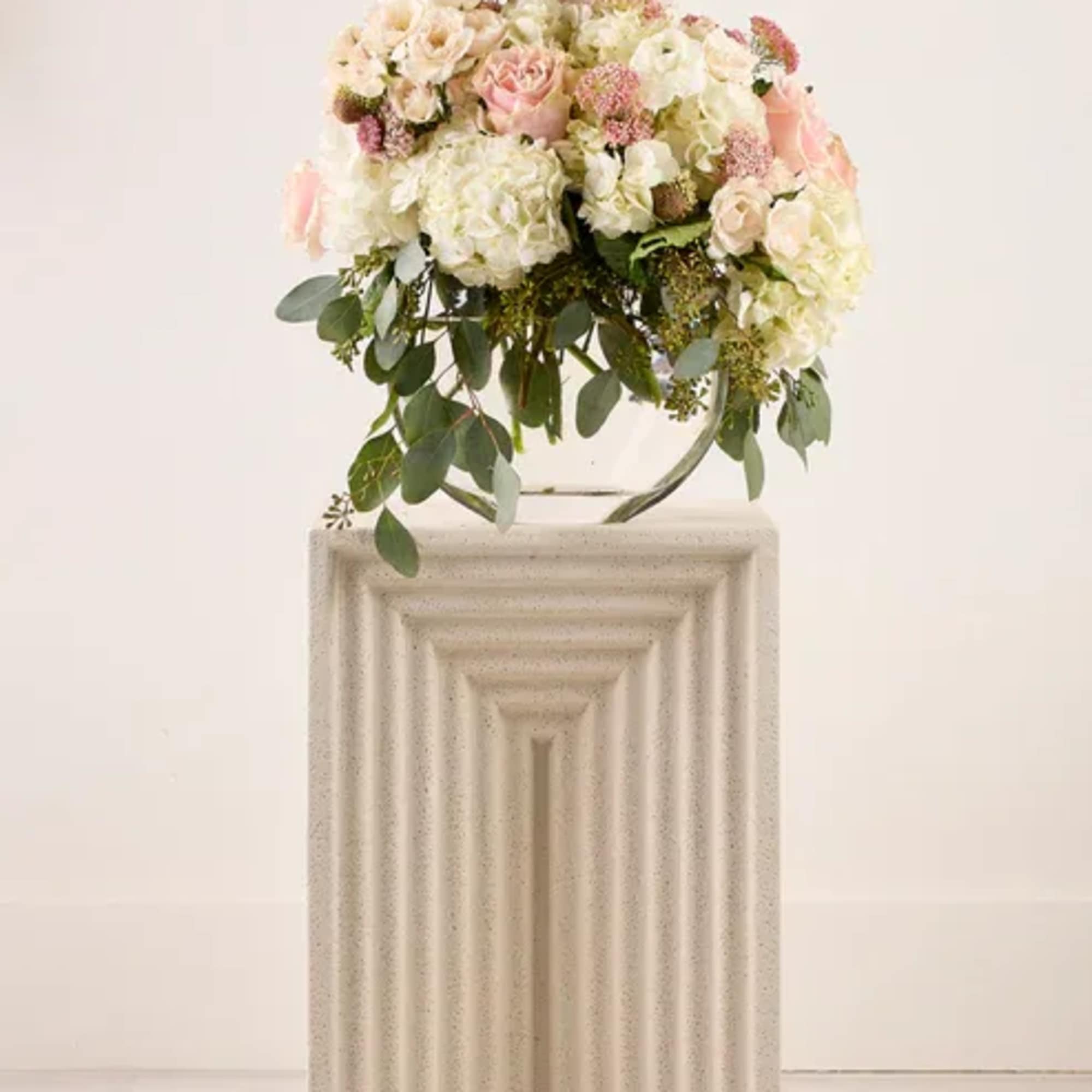 Blush and white floral arrangement on a pedestal with trailing greenery