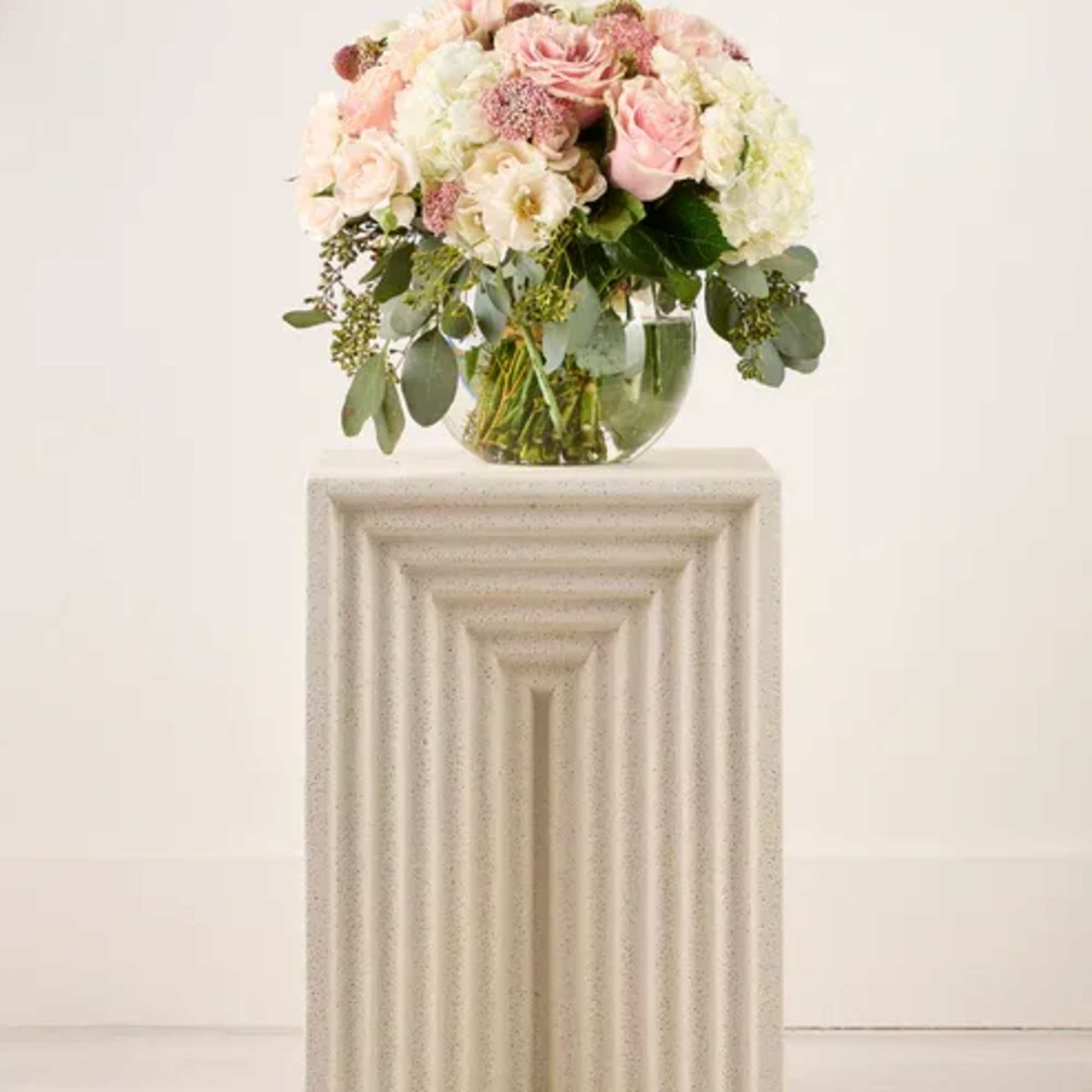 Blush and white floral arrangement in a clear glass vase on a pedestal