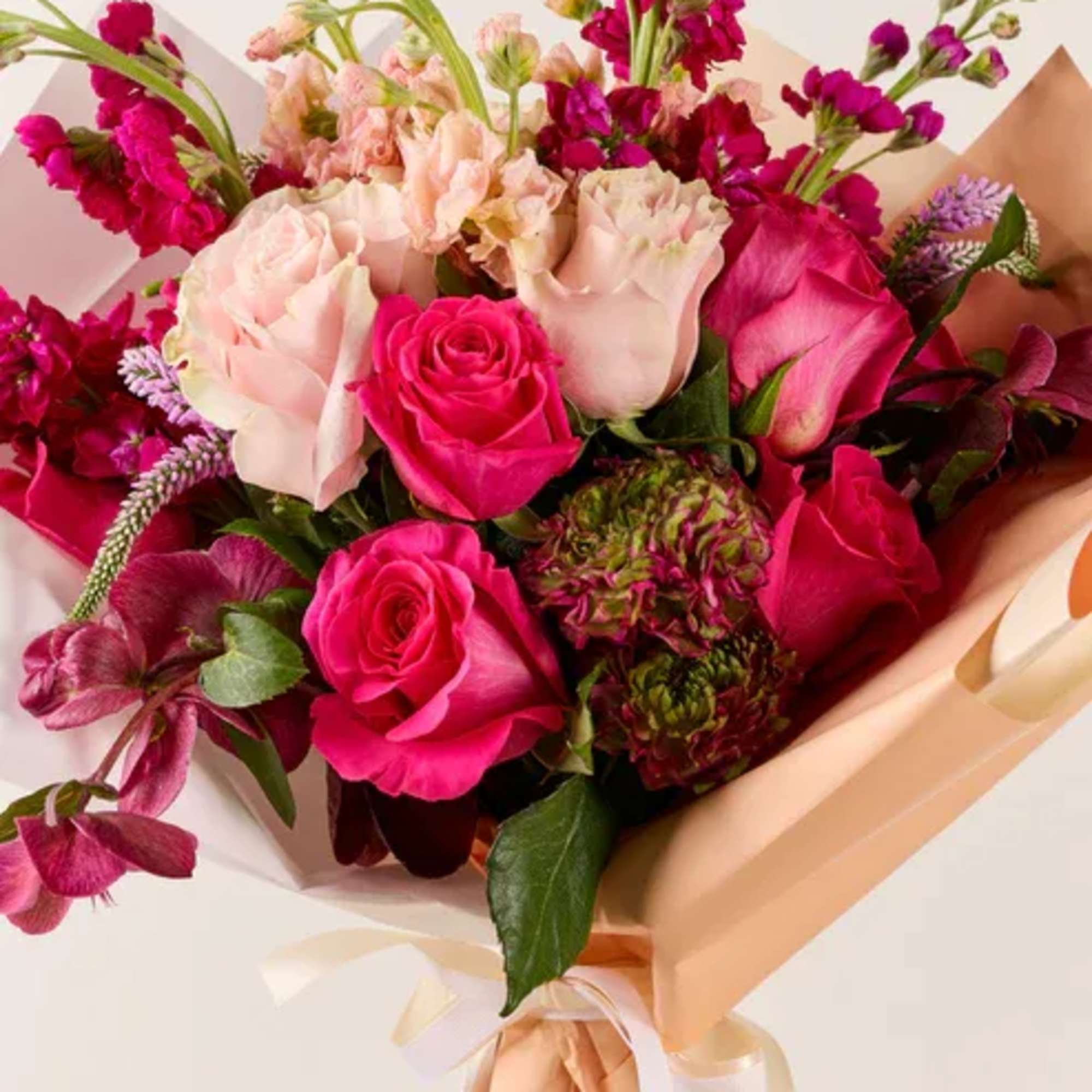 Bouquet of pink and blush roses with magenta blooms wrapped in peach paper