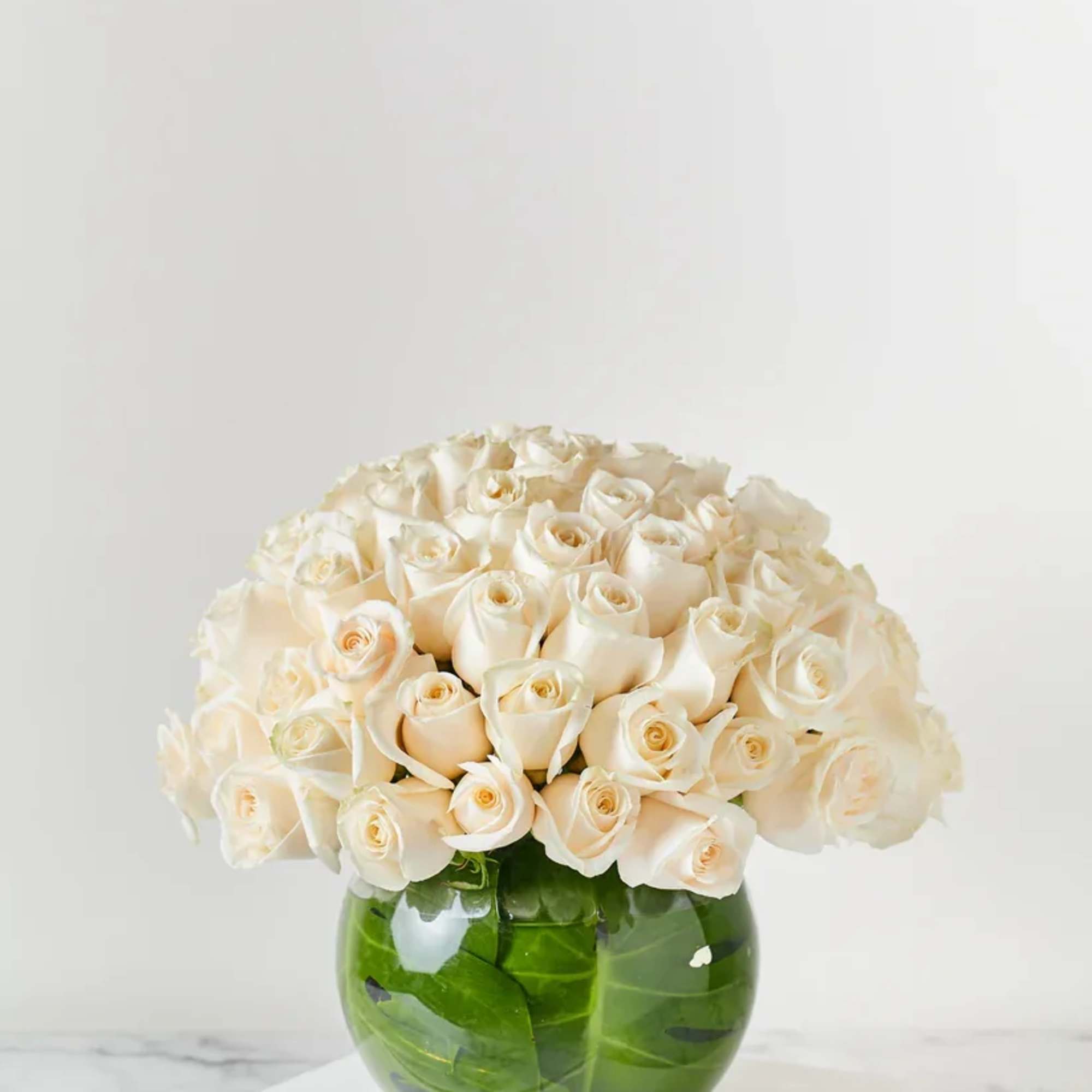 Cream roses arranged in a round green glass vase