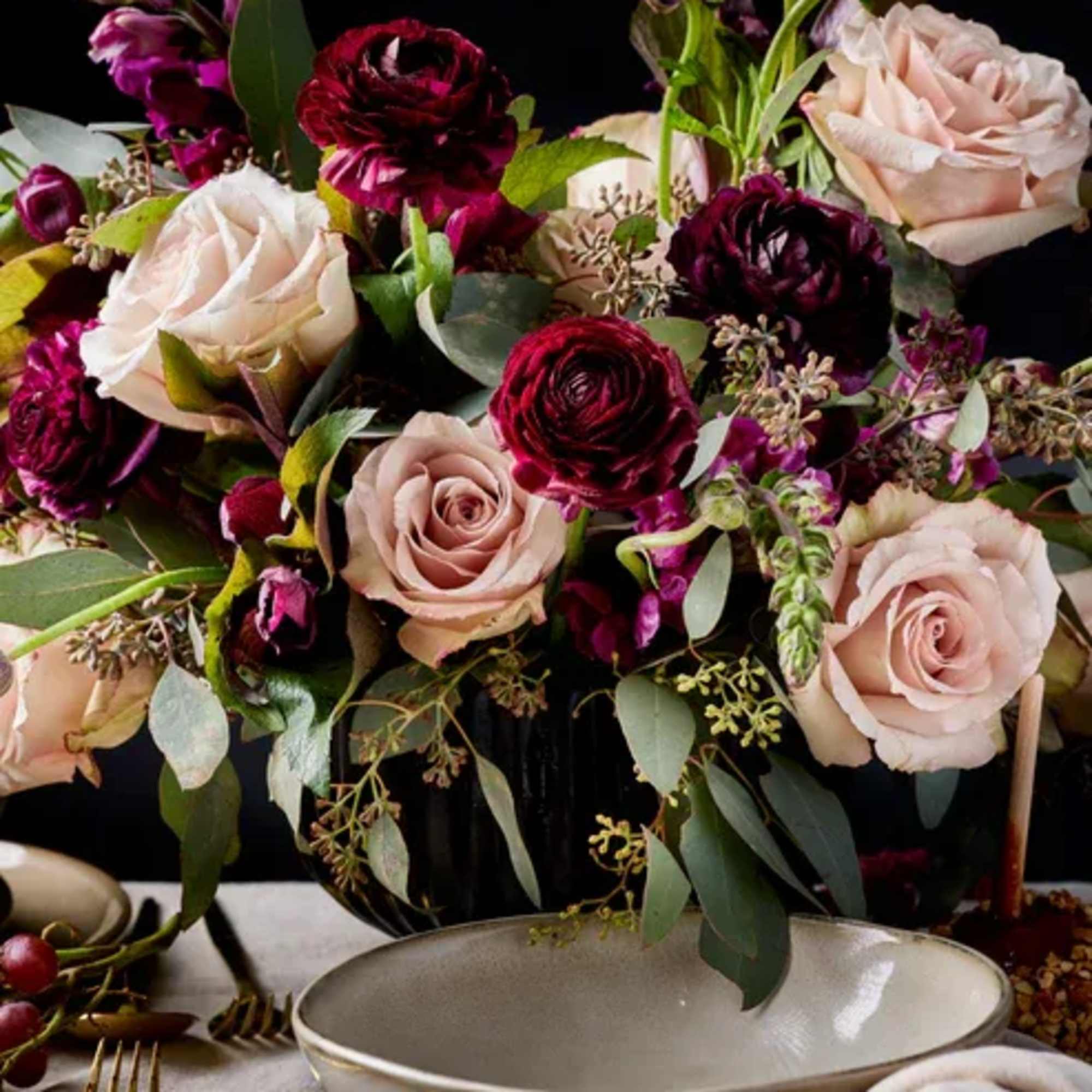 Blush and burgundy roses arranged in a low centerpiece with greenery