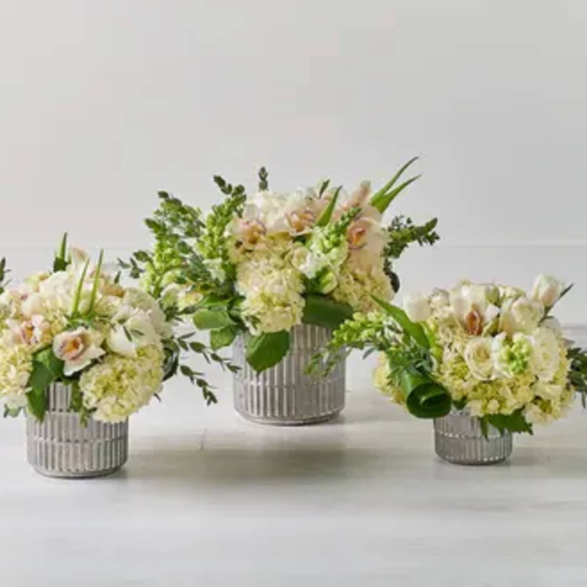 Three pale floral arrangements in ribbed silver containers