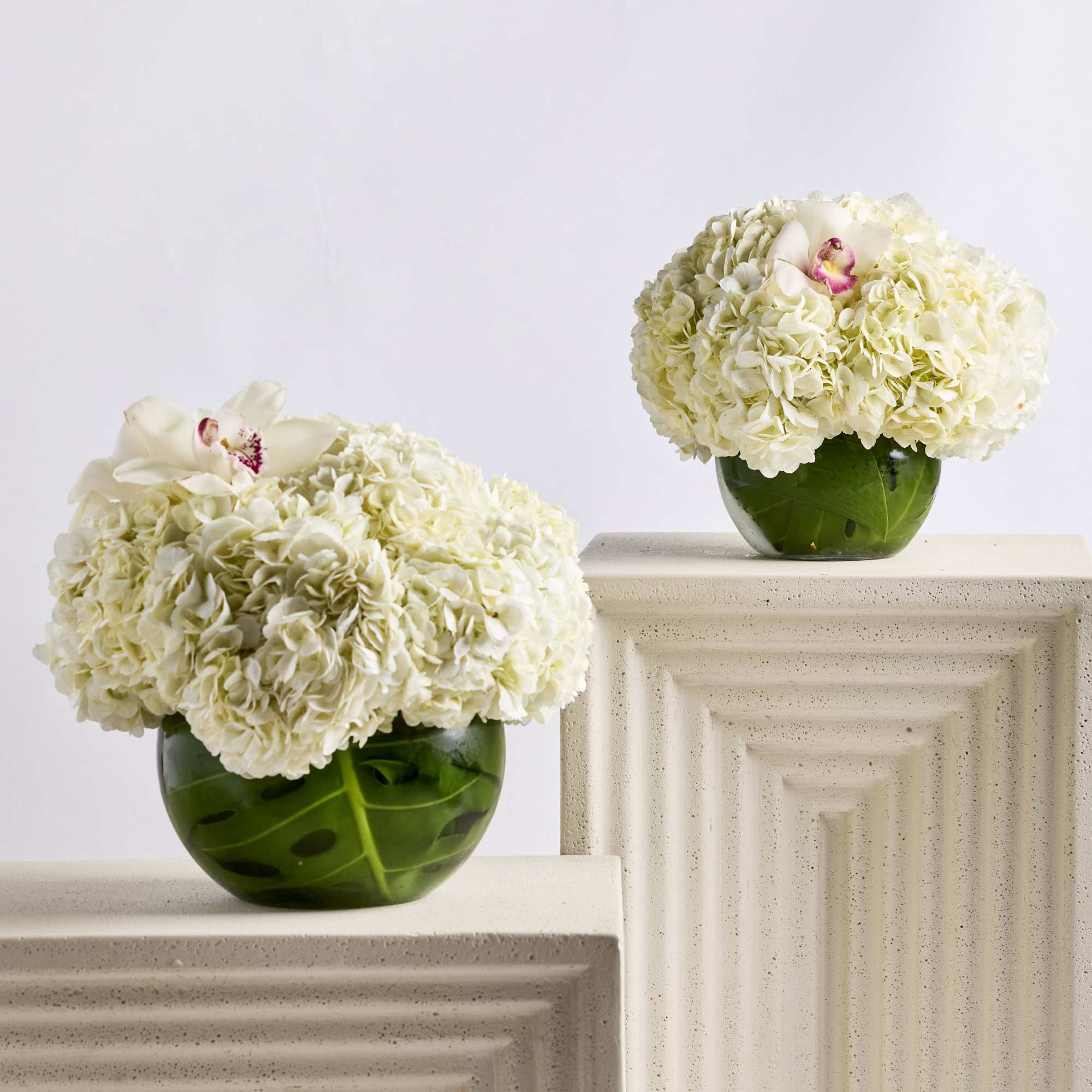 Two white hydrangea arrangements in green glass vases on pedestals