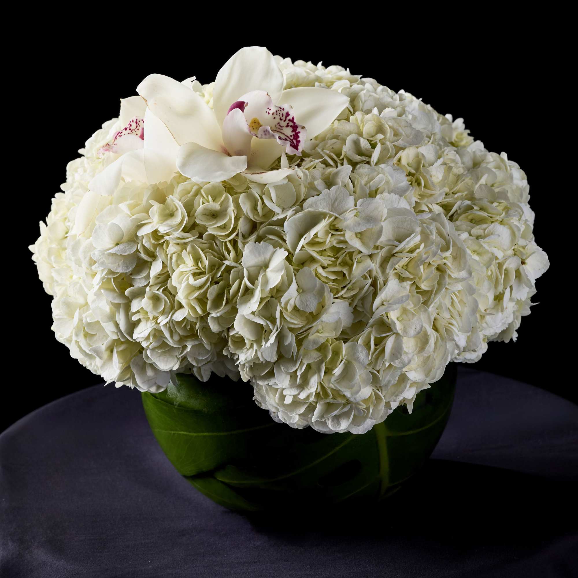 White hydrangea arrangement with white orchids in a green vase