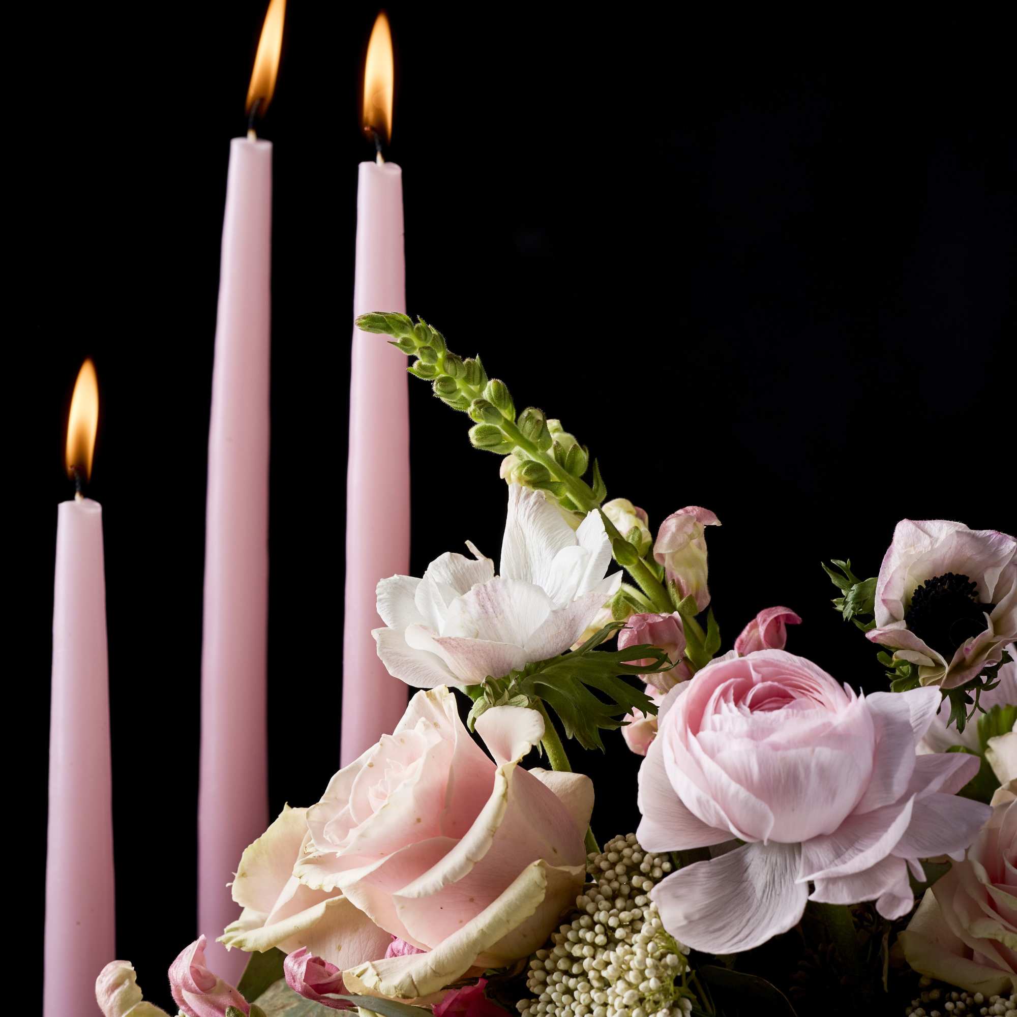 Pink candles beside a pastel bouquet of roses and anemones