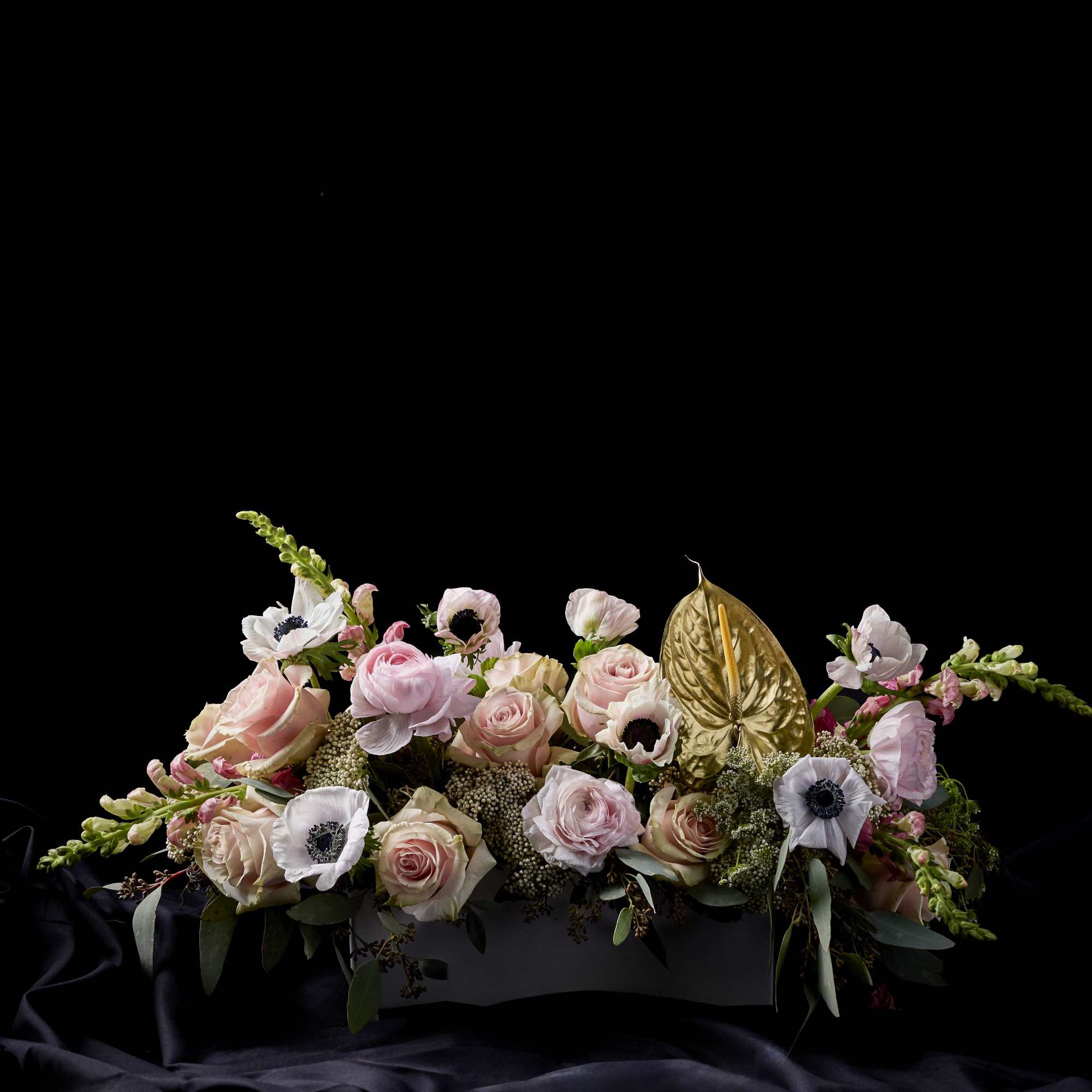 Pastel floral arrangement with roses, anemones, and a gold anthurium leaf