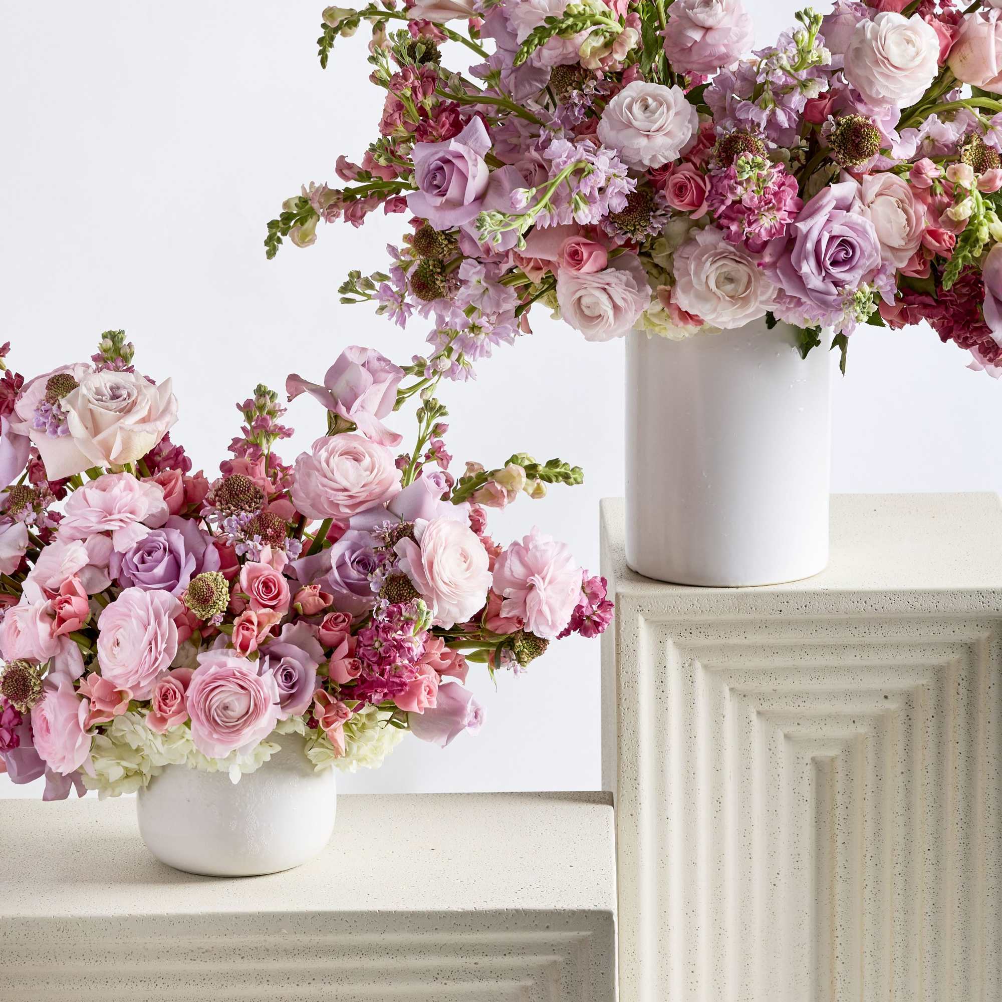Two pink floral arrangements in white vases on textured pedestals