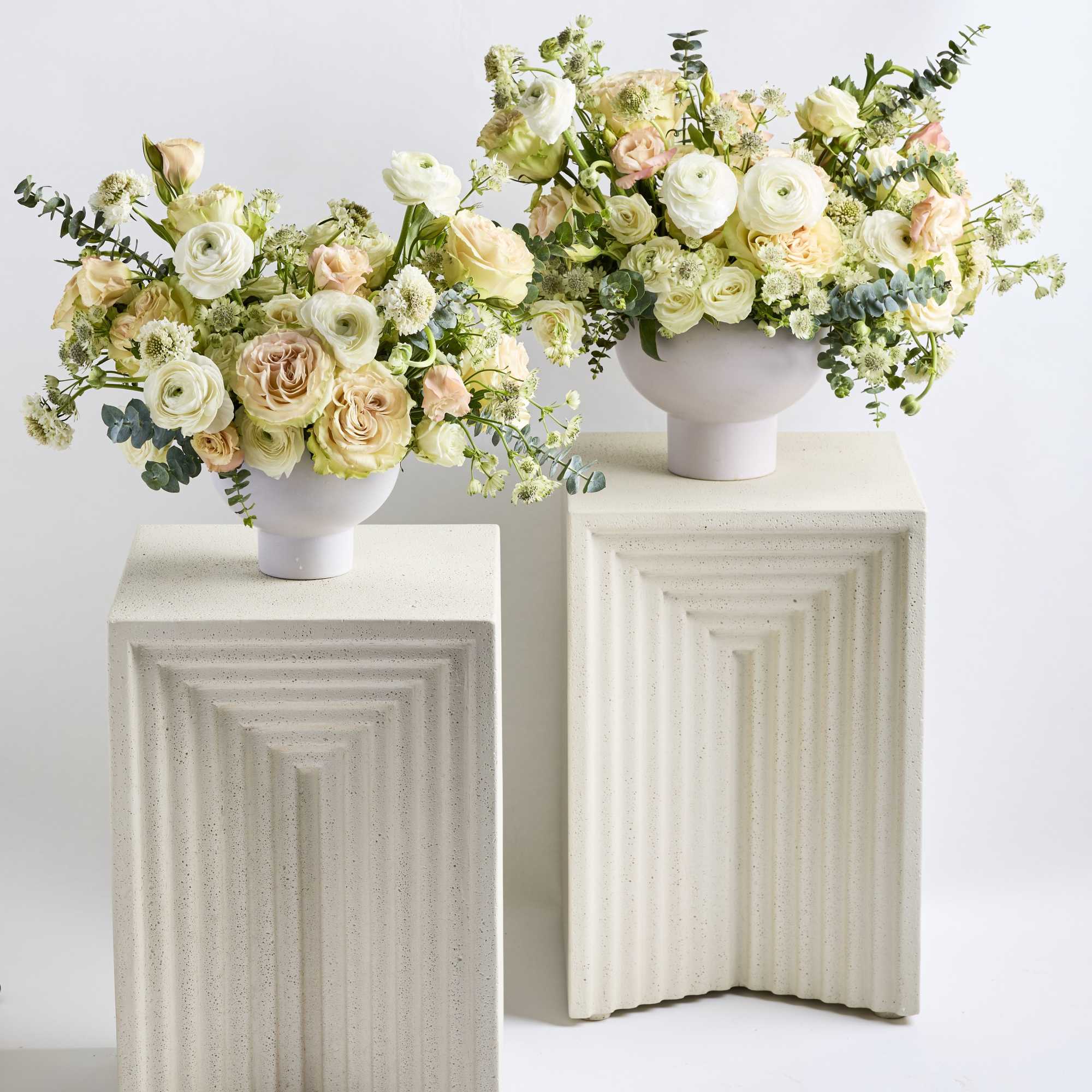 Two pastel floral arrangements in white pedestal vases