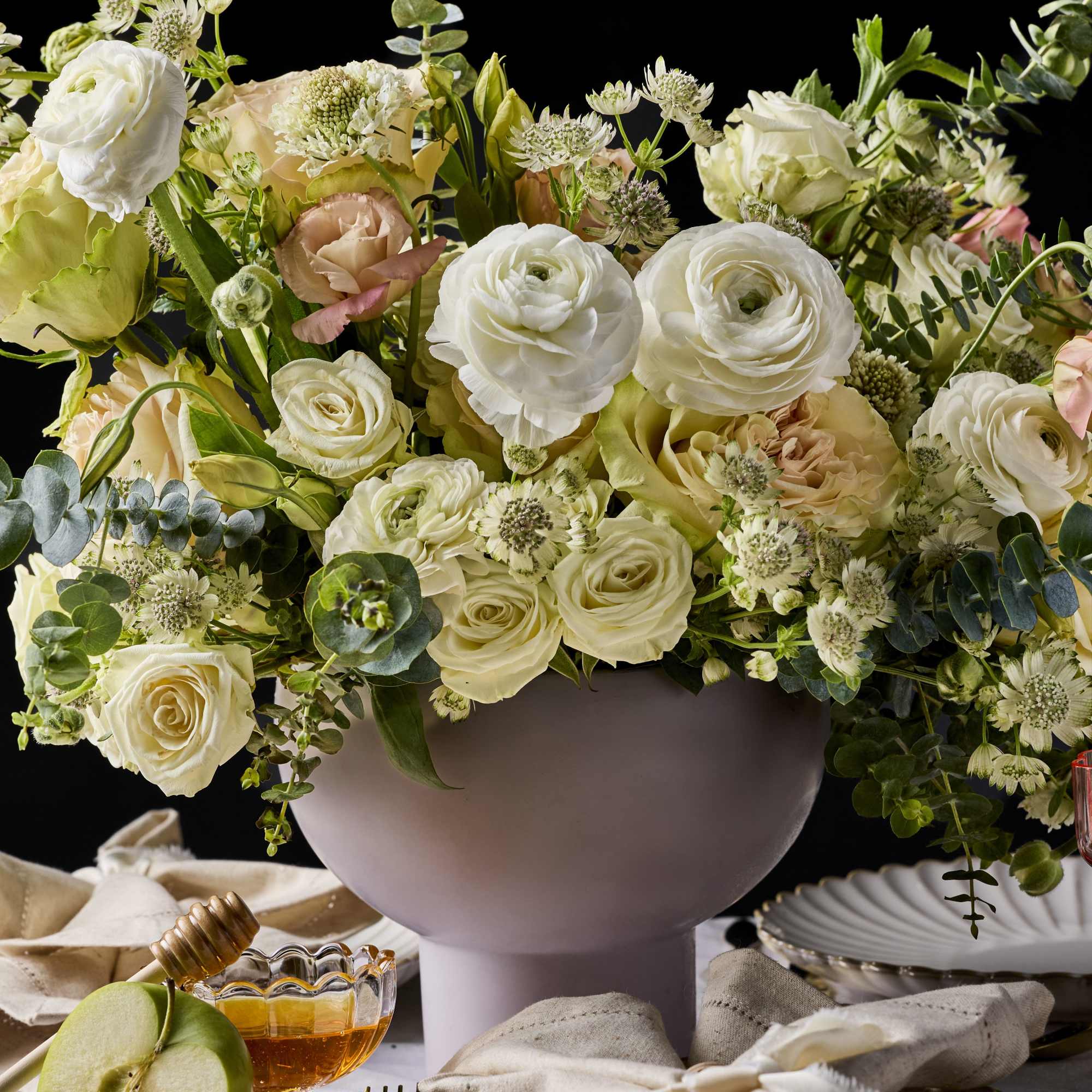Cream and blush roses in a lavender vase with table settings and fruit